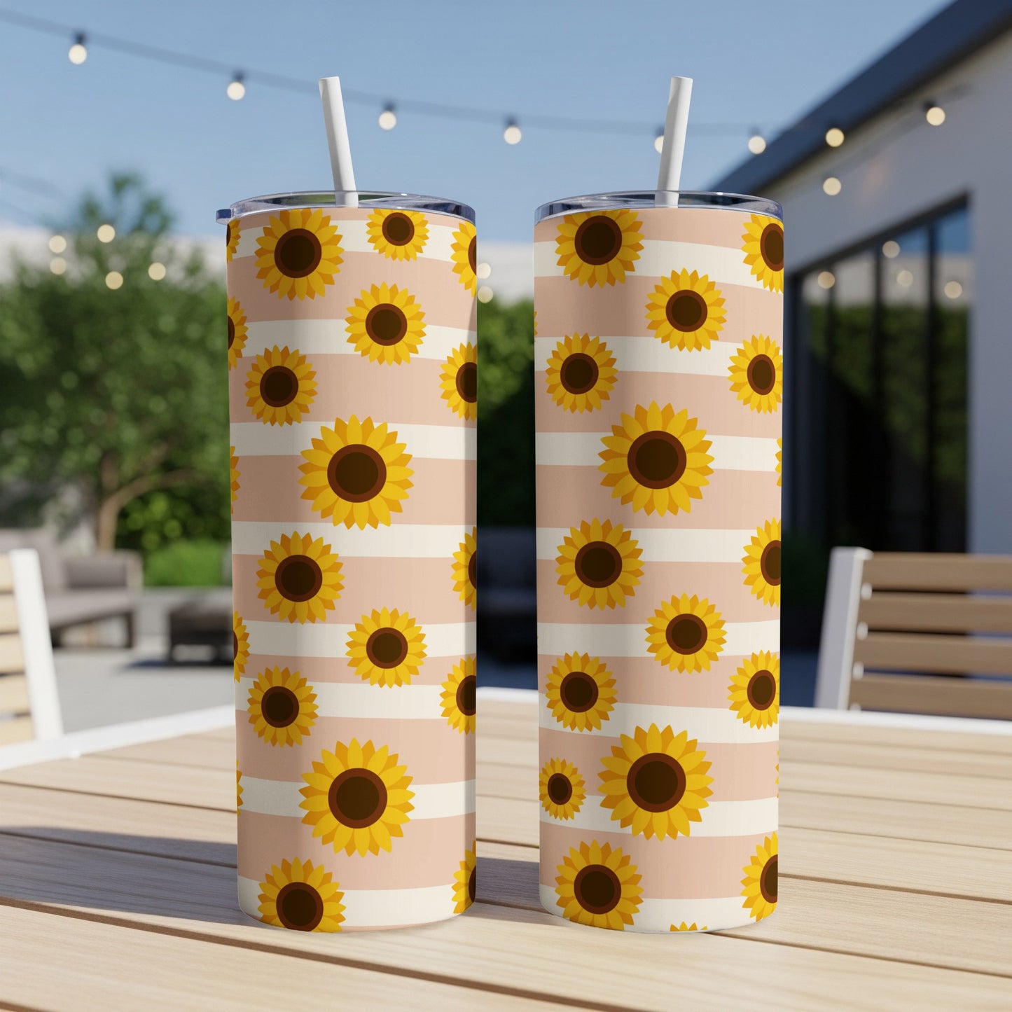 Two tumblers with a sunflower and stripe pattern sit on a wooden table outdoors.