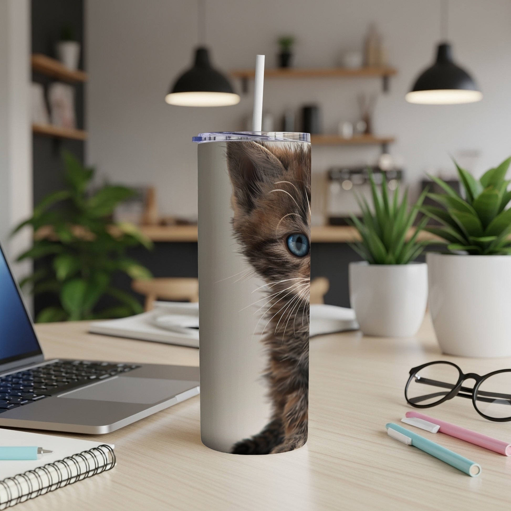 Tabby kitten with blue eyes peeking from a tumbler on a desk.