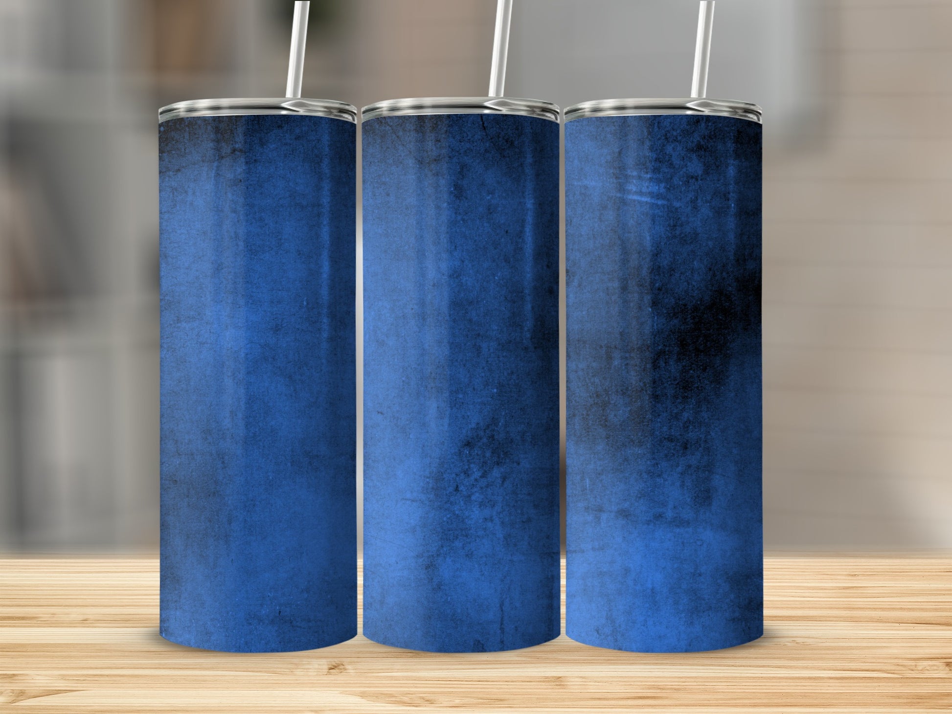 Three blue tumblers with textured grunge design and straws on wooden surface.