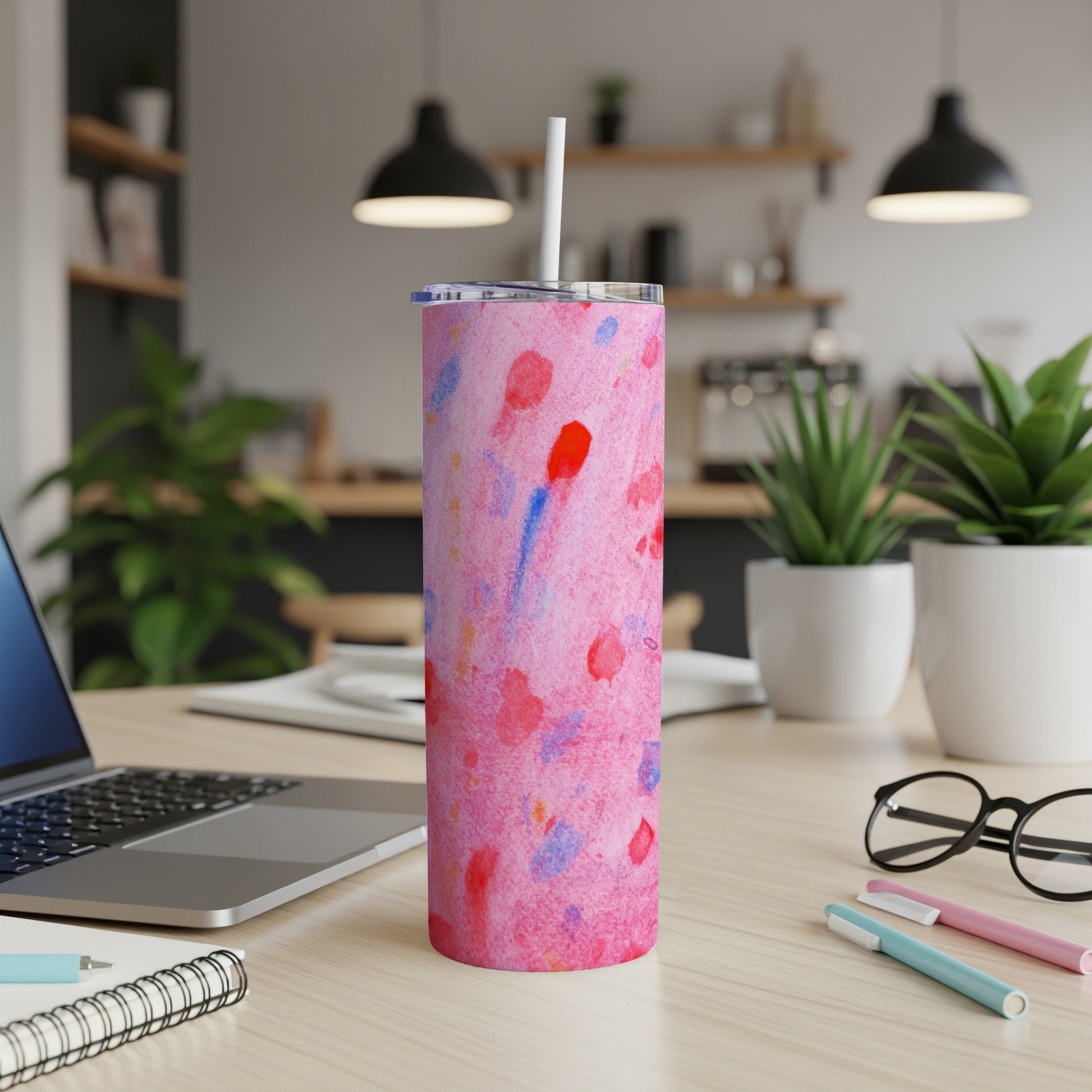 Pink and blue watercolor pattern tumbler with white lid and straw on desk.