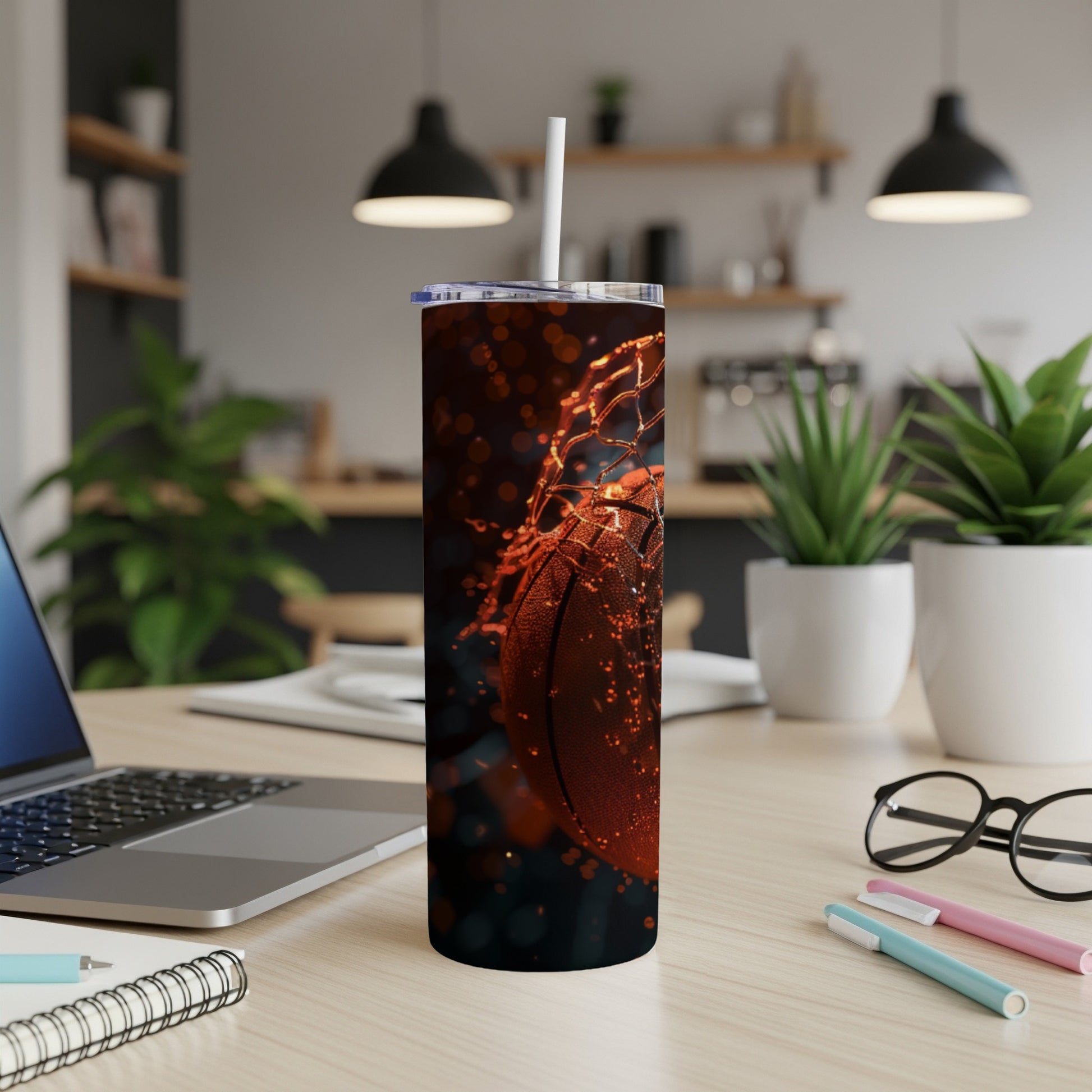 Basketball in net with straw in tumbler, laptop and glasses on desk.