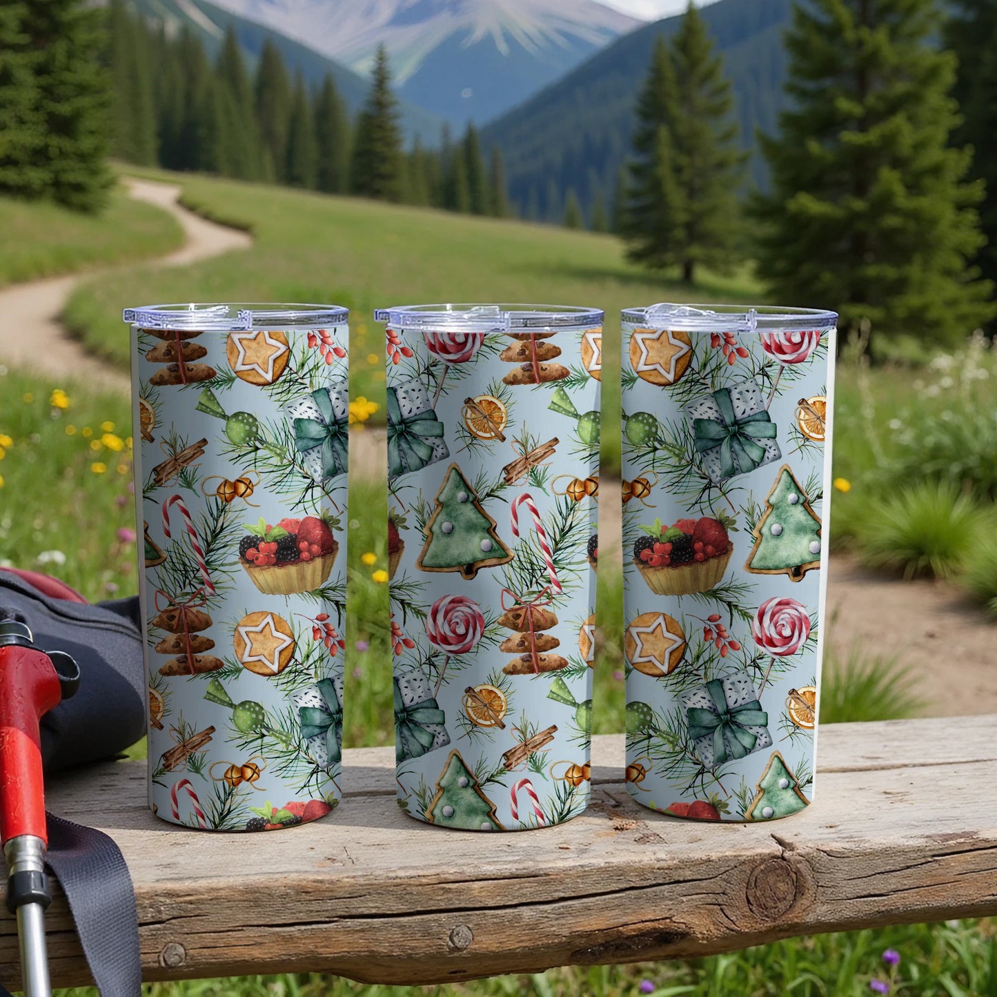 Three tumblers with Christmas patterns sit on a wooden table outdoors.