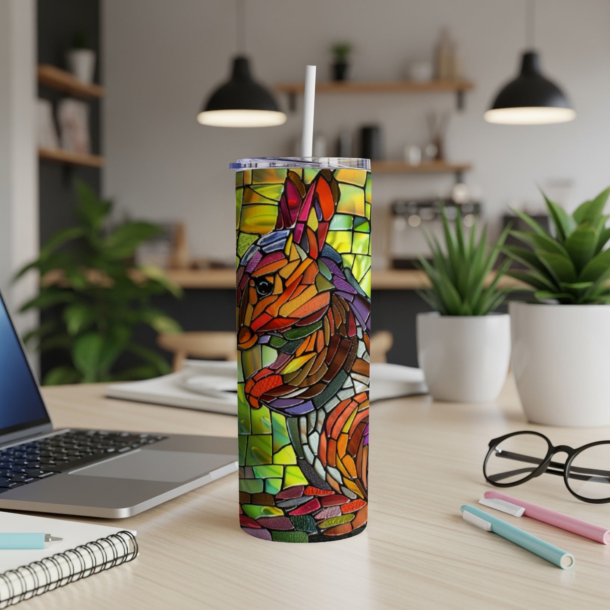 Stained glass rabbit tumbler with straw on desk with laptop and pens.