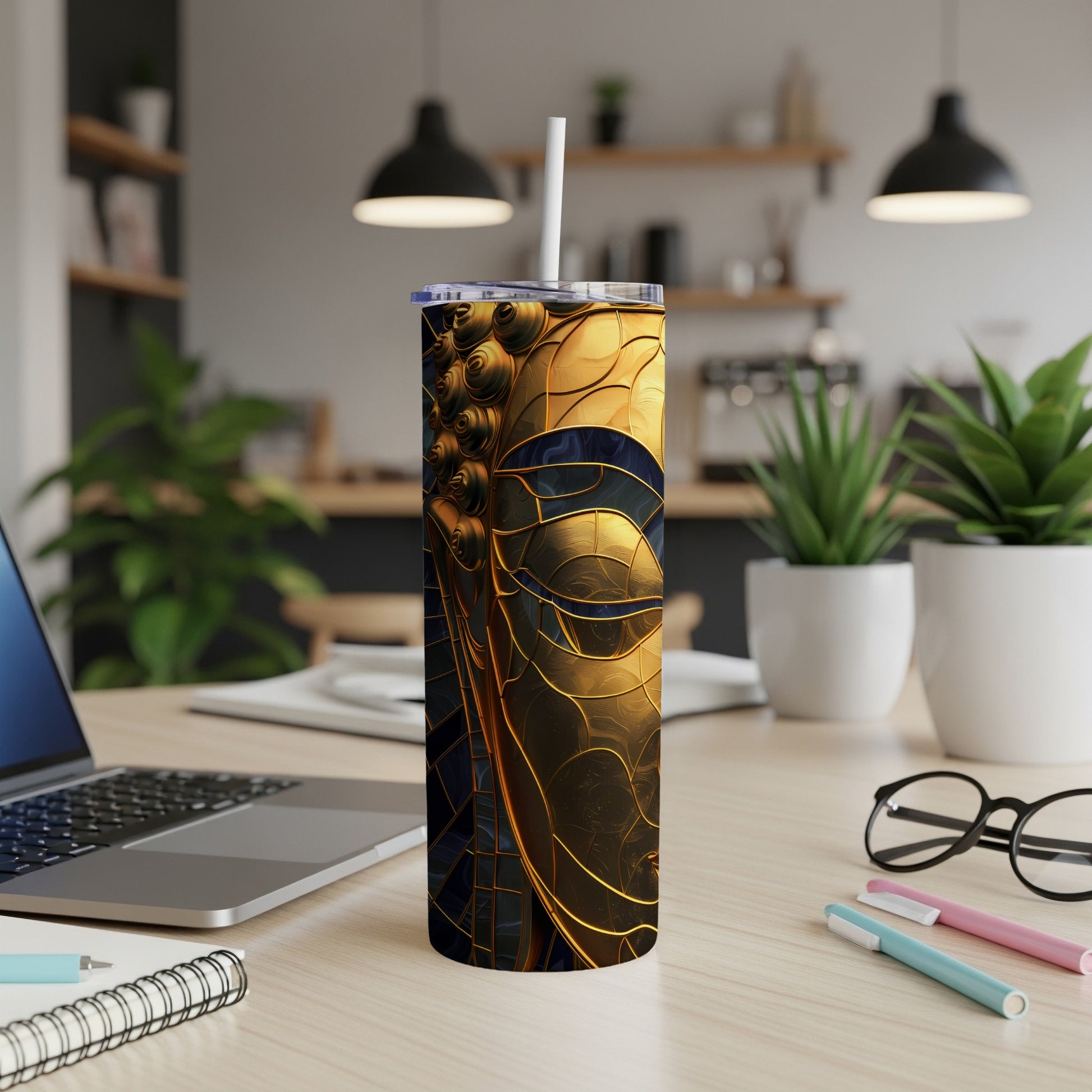 Gold and blue abstract patterned tumbler on a desk with laptop and pens.