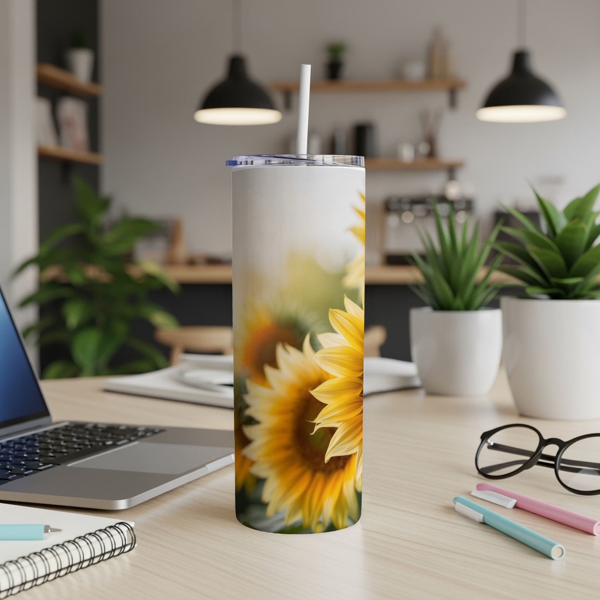 Sunflower tumbler with straw on desk with laptop and pens.