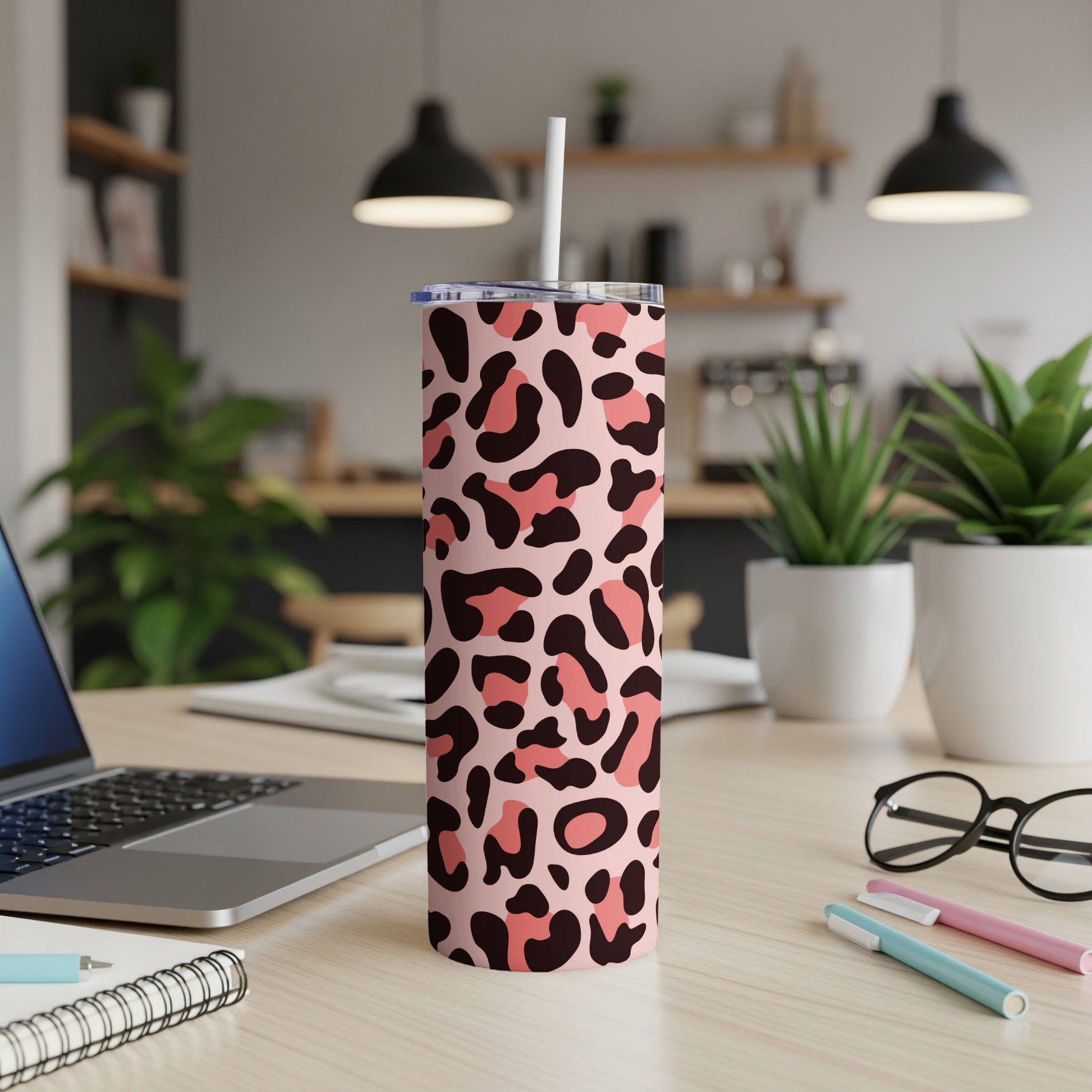 Pink leopard print tumbler with straw on a desk with laptop and plants.