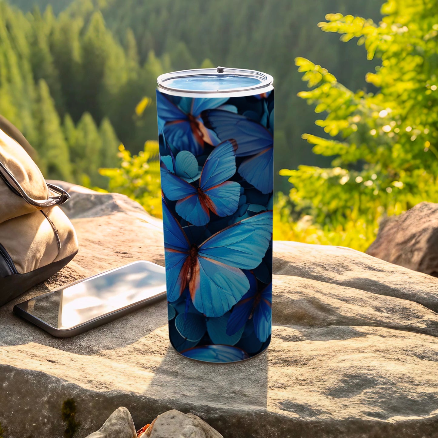 Blue butterfly pattern on a stainless steel tumbler resting on rocks.