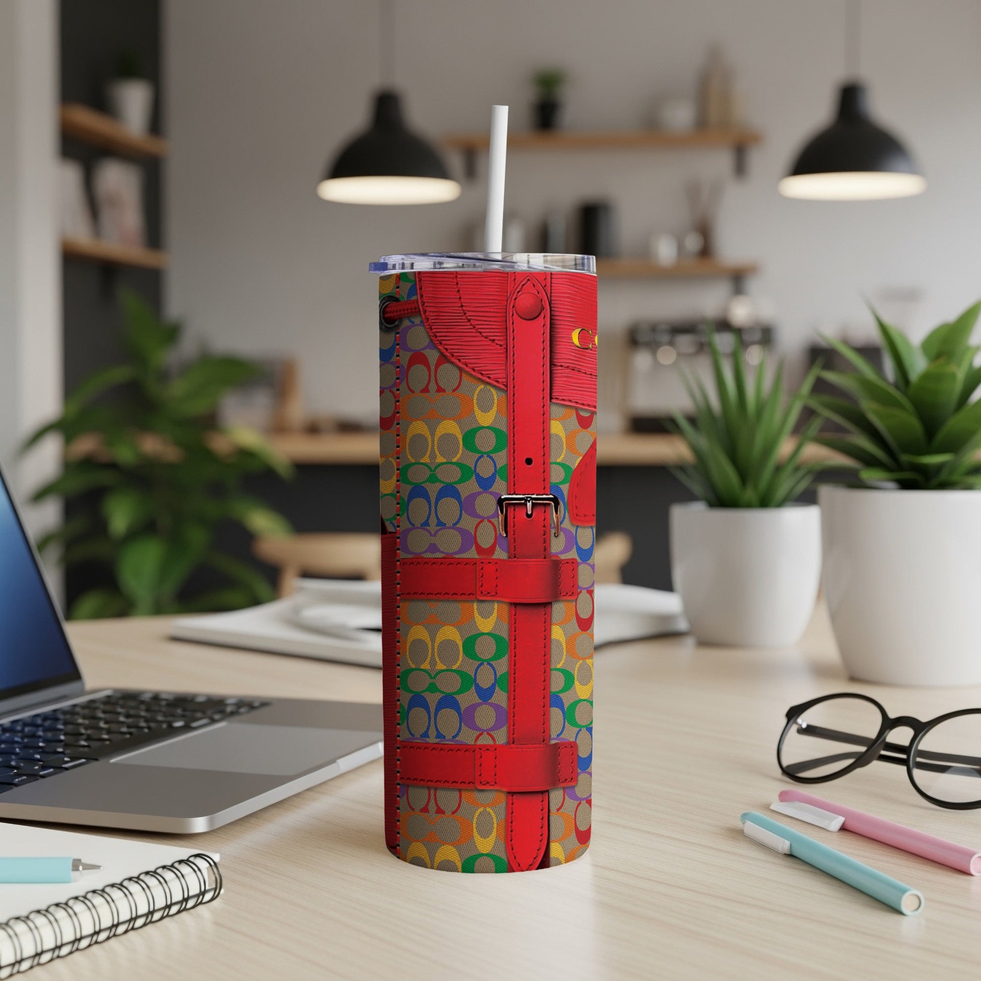 Tumbler with rainbow C pattern and red strap details on a desk.