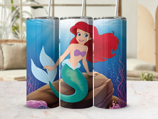 Ariel the Little Mermaid sits on a rock underwater with a colorful coral reef background.