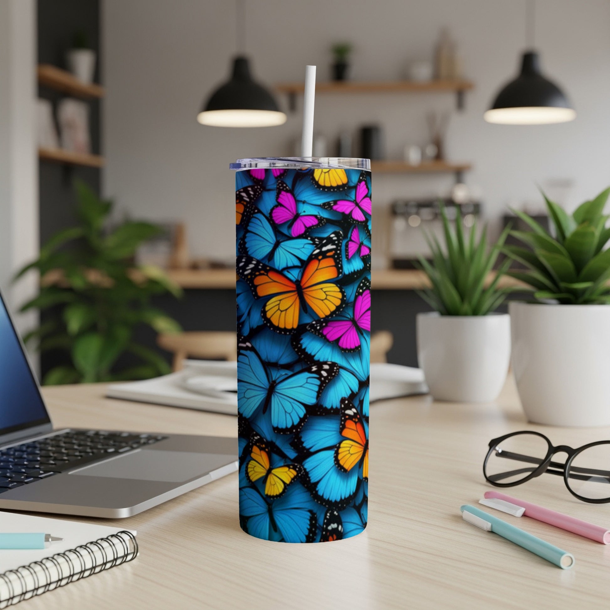 Blue tumbler with colorful butterflies, straw inserted, on a desk.