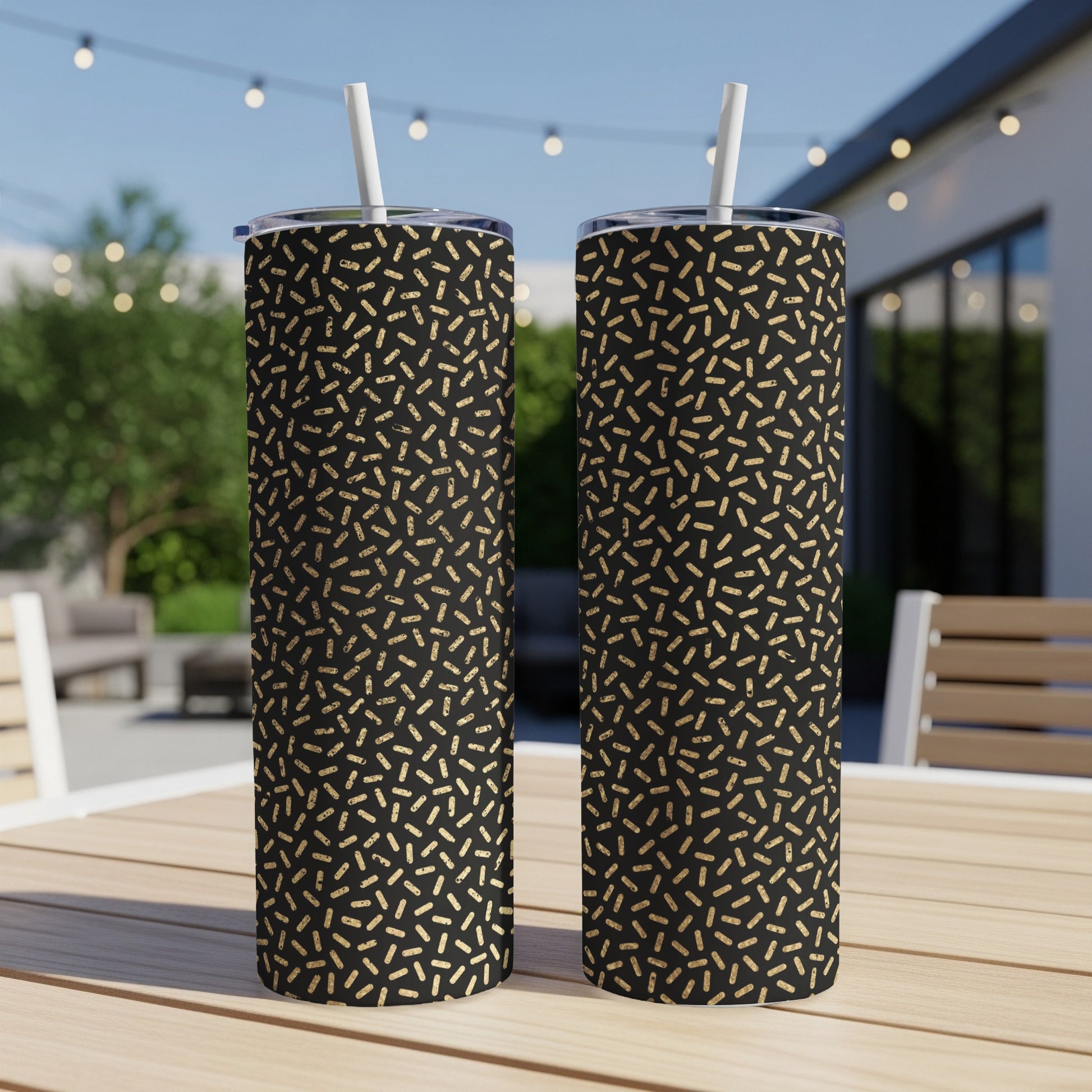 Two black tumblers with gold sprinkle pattern and white straws on a table.