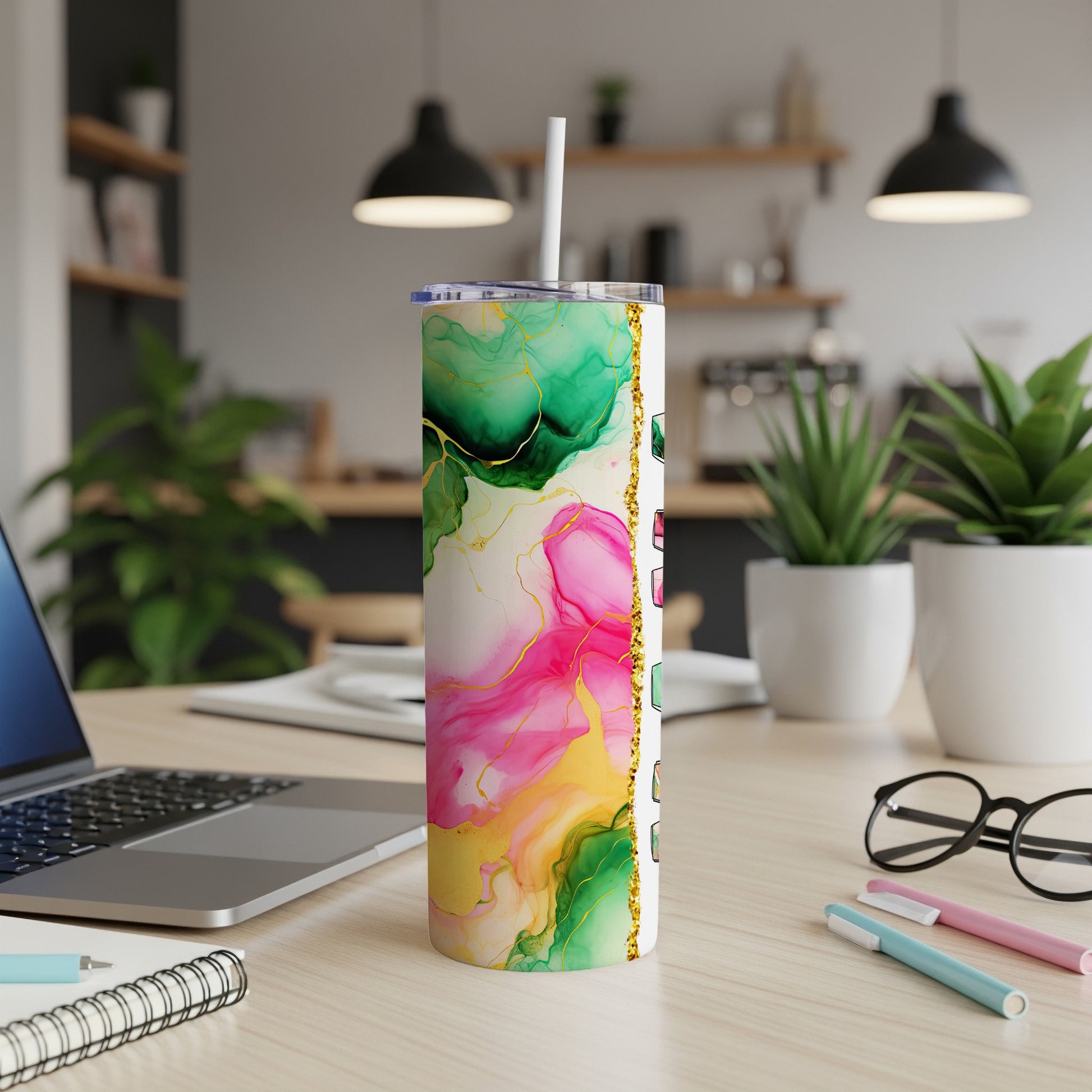 Pink, green, and gold abstract marble tumbler with straw on desk.