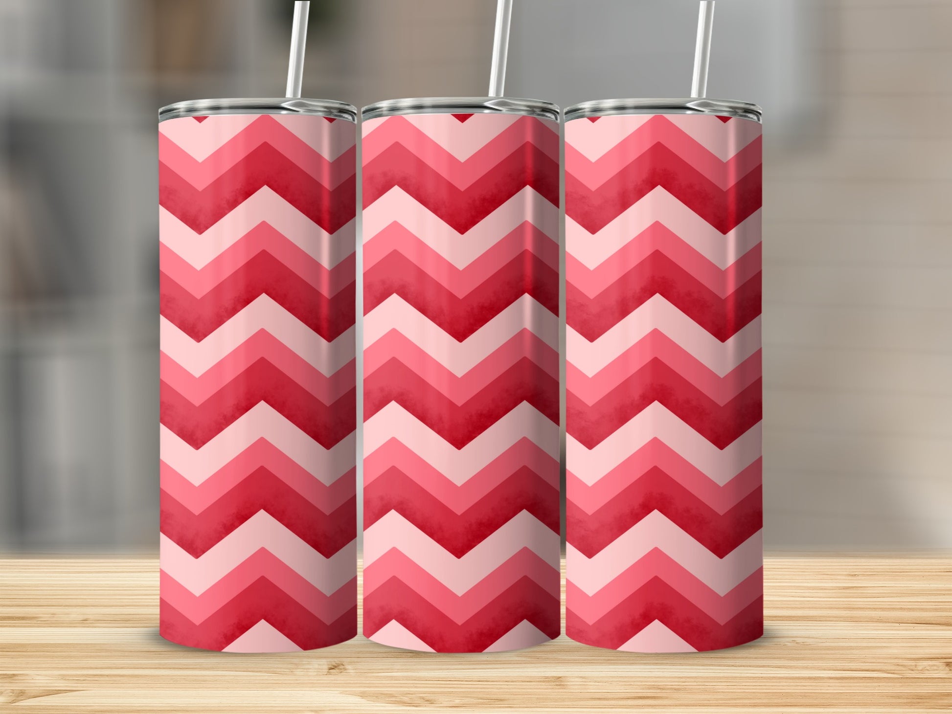 Three pink and red chevron patterned tumblers with straws on a wooden surface.