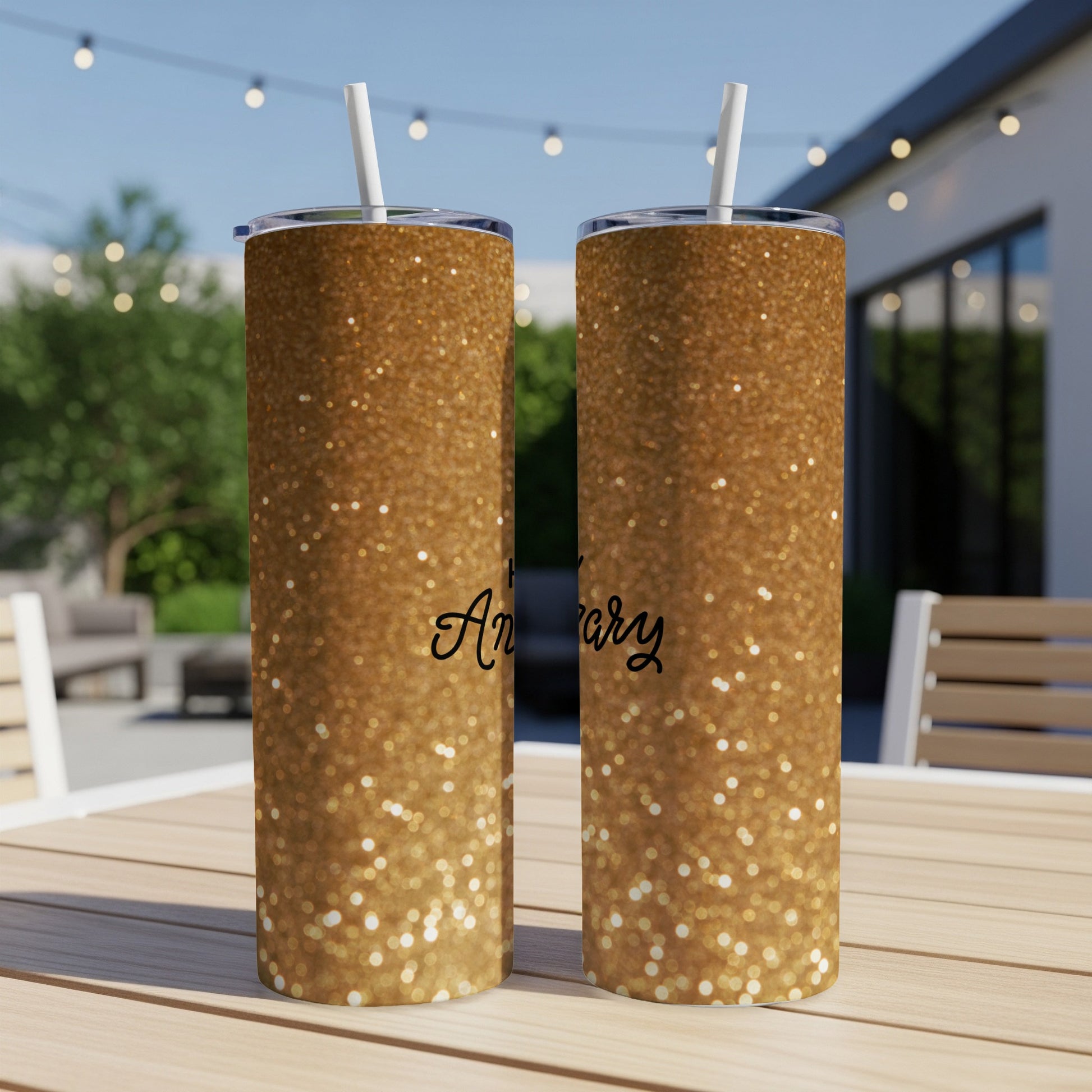 Gold glitter tumbler with "Anniversary" text, on an outdoor table.