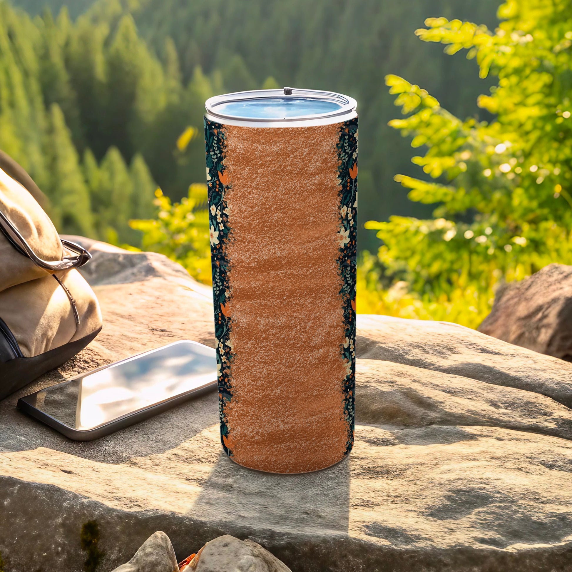 Patterned tumbler with floral and leaf accents on a rocky, outdoor surface.