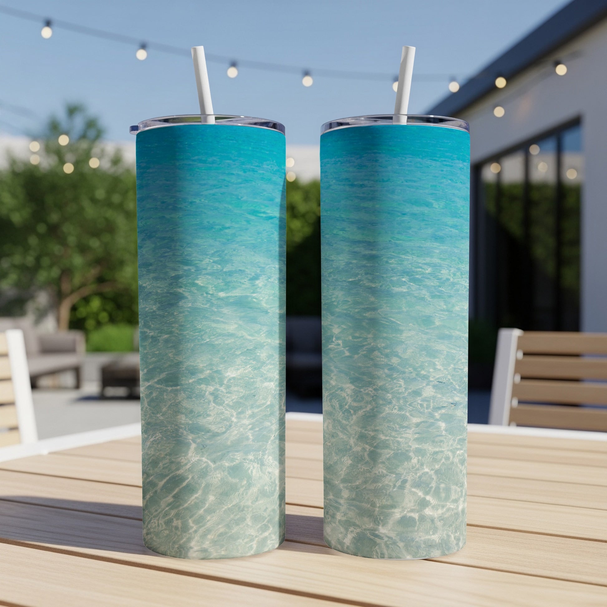Two blue and white tumblers with straws on a wooden table outdoors.
