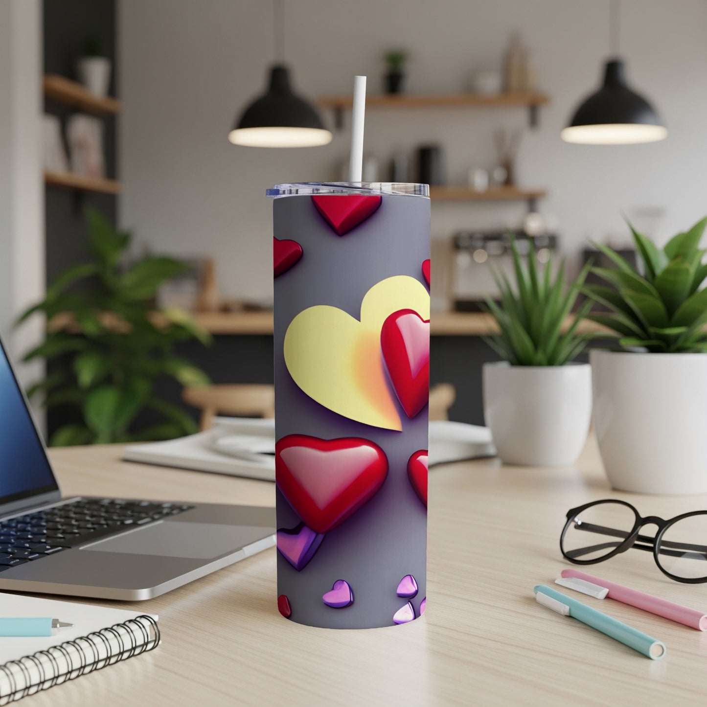 Gray tumbler with red and yellow hearts, straw, on a desk.