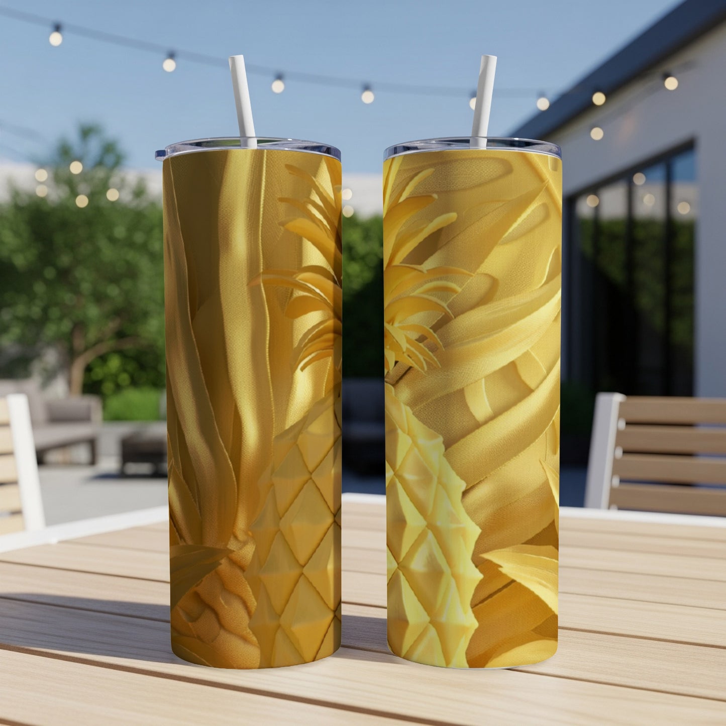 Two gold tumblers with pineapple designs on a wooden table outdoors.