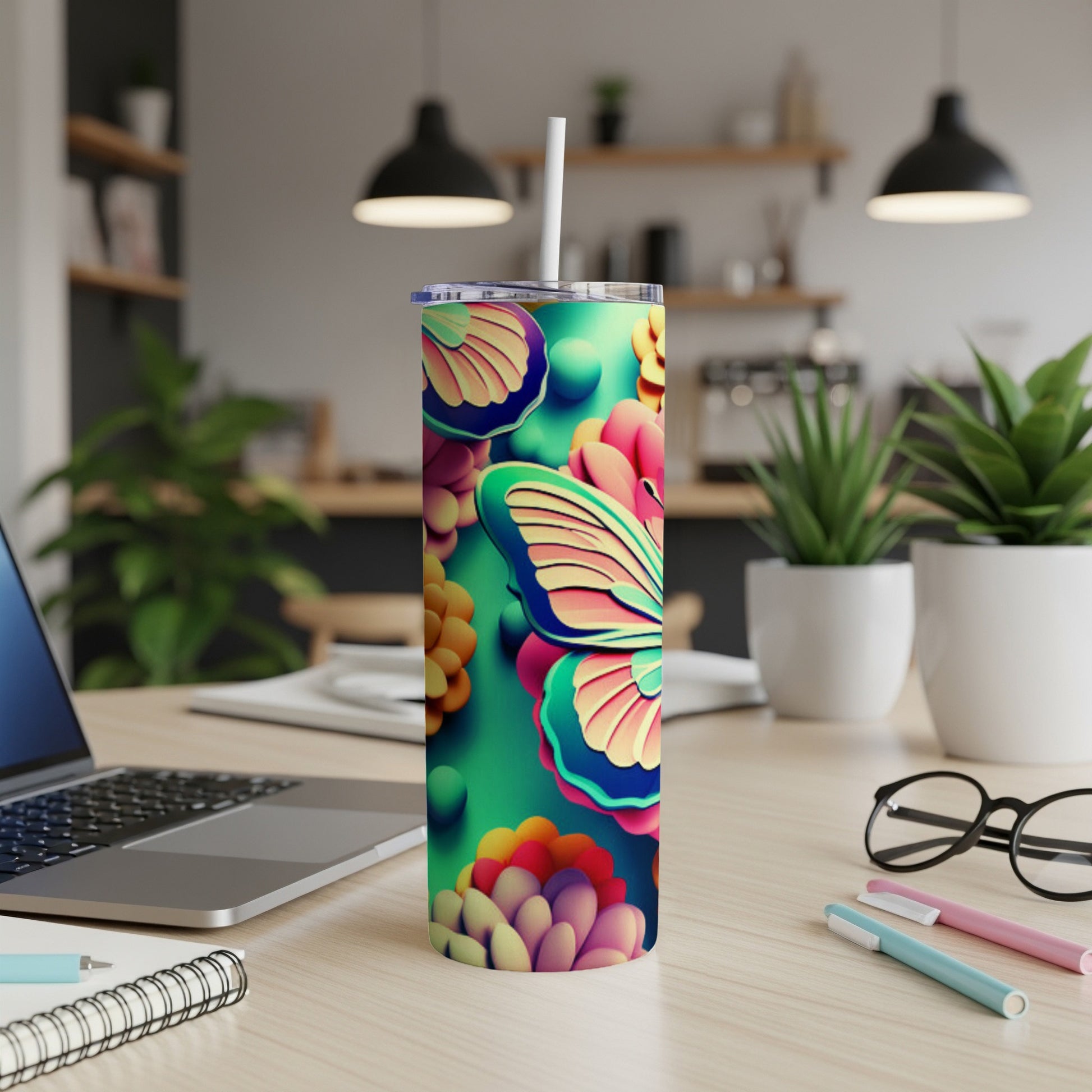 Butterfly and floral patterned tumbler with a straw, on a desk.
