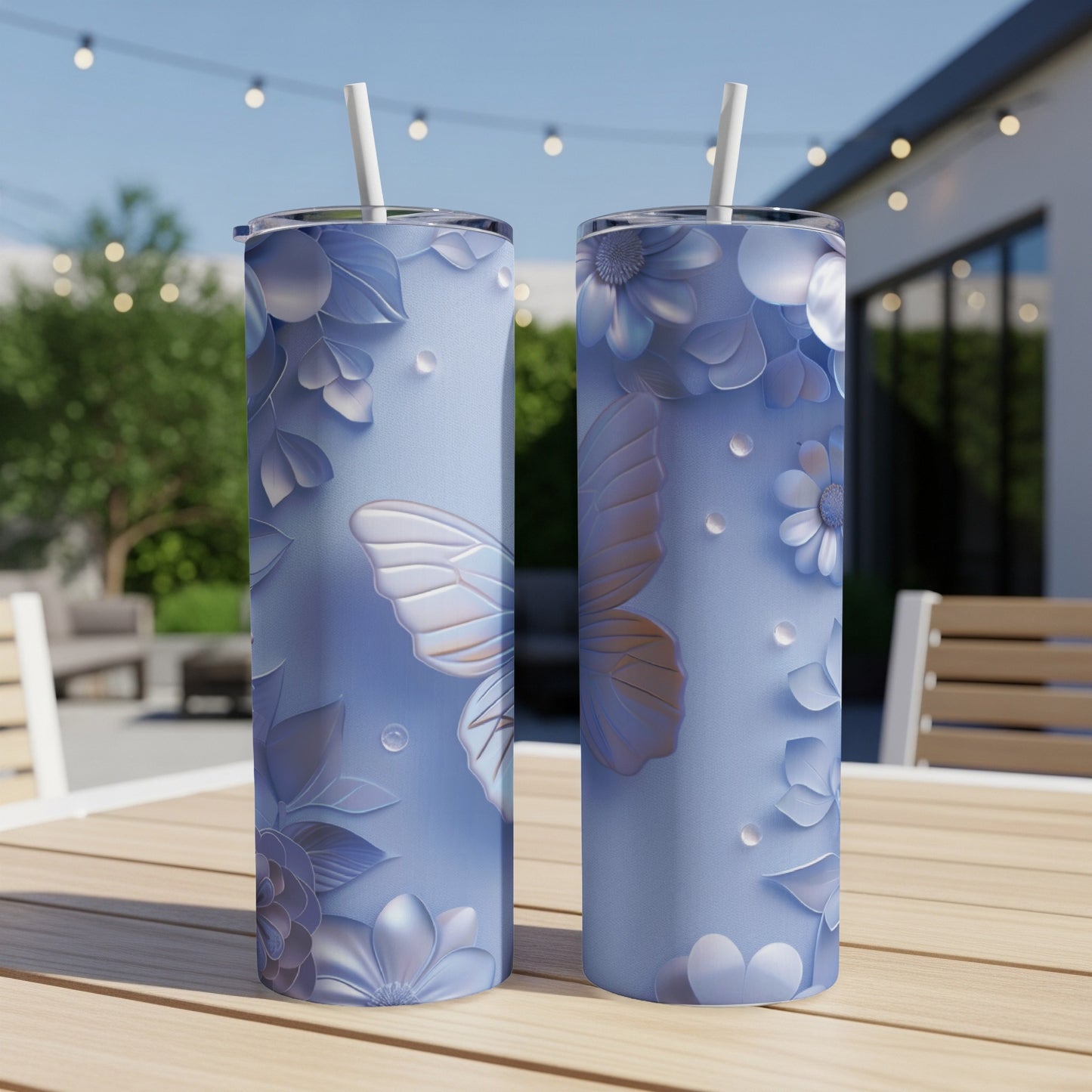 Two light blue tumblers with butterfly and floral design sit on a wooden table outdoors.