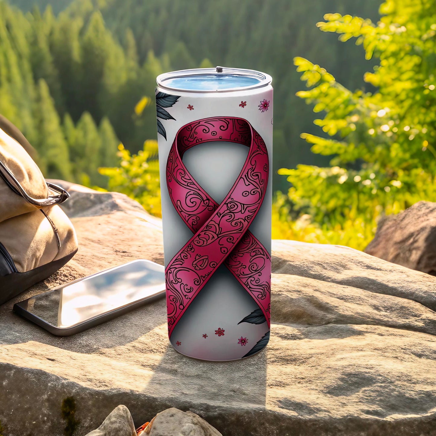 Pink ribbon tumbler with floral pattern on a rock outdoors.