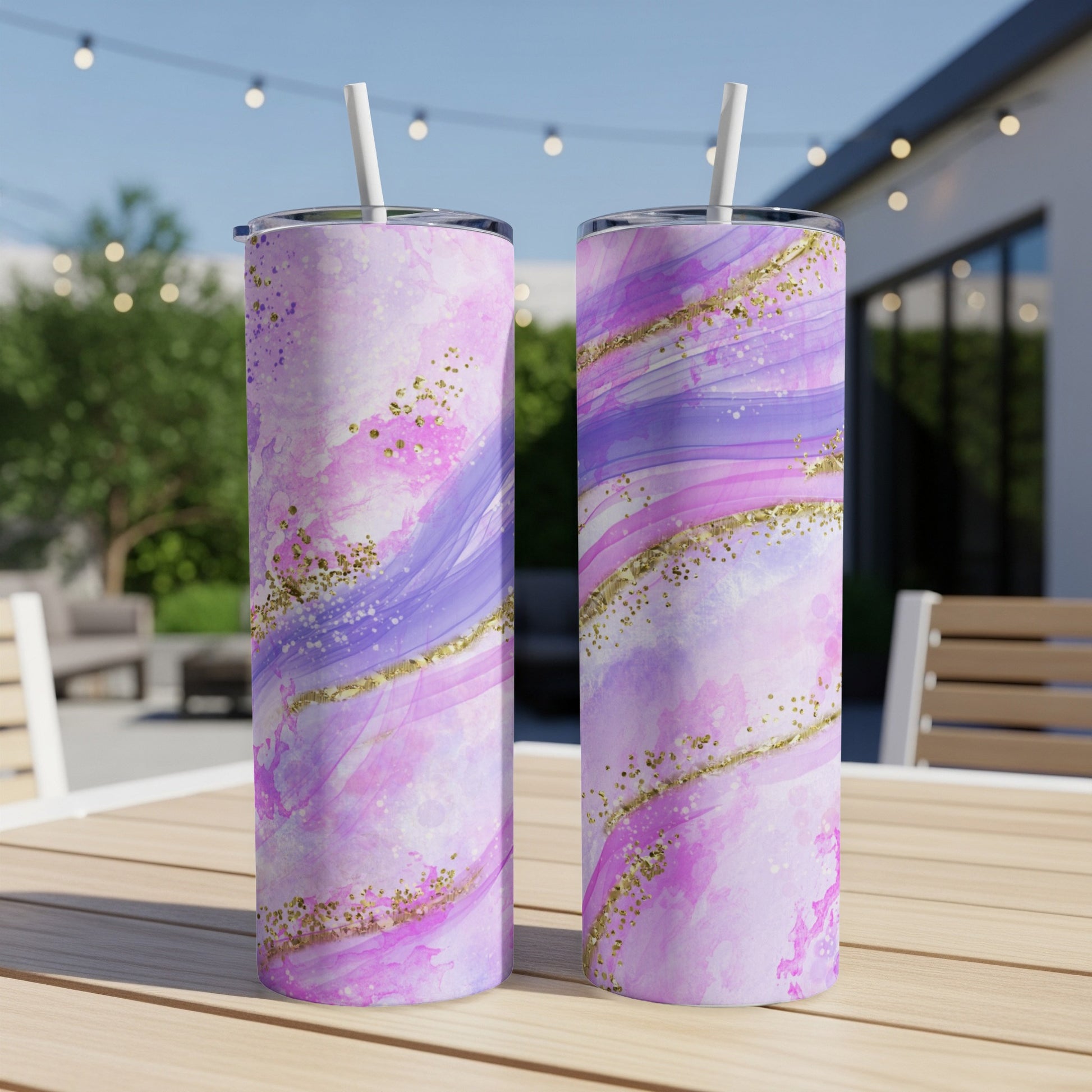 Two purple and pink marbled tumblers with gold glitter accents sit on a wooden table.