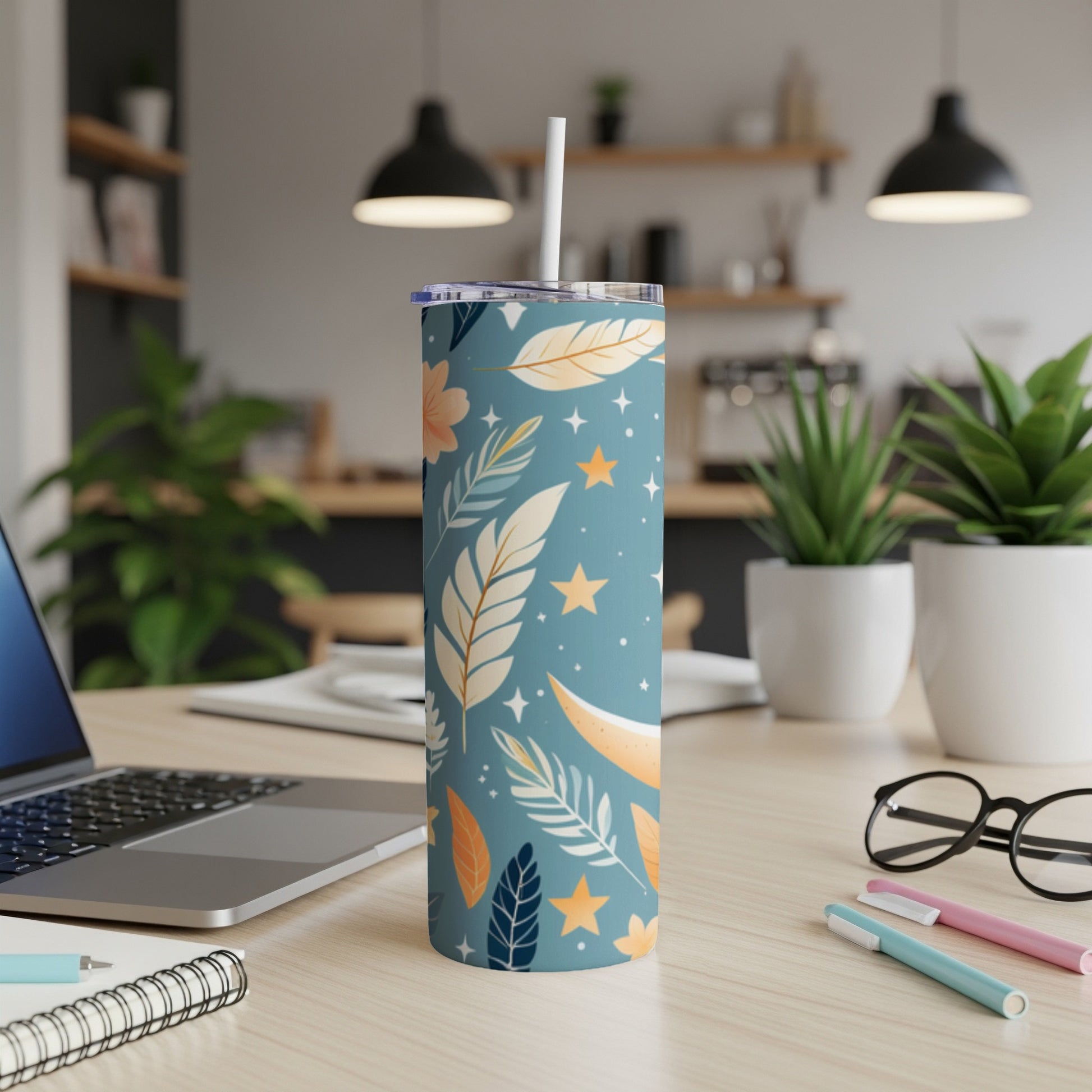 Blue tumbler with floral and star pattern, straw, and pens on desk.