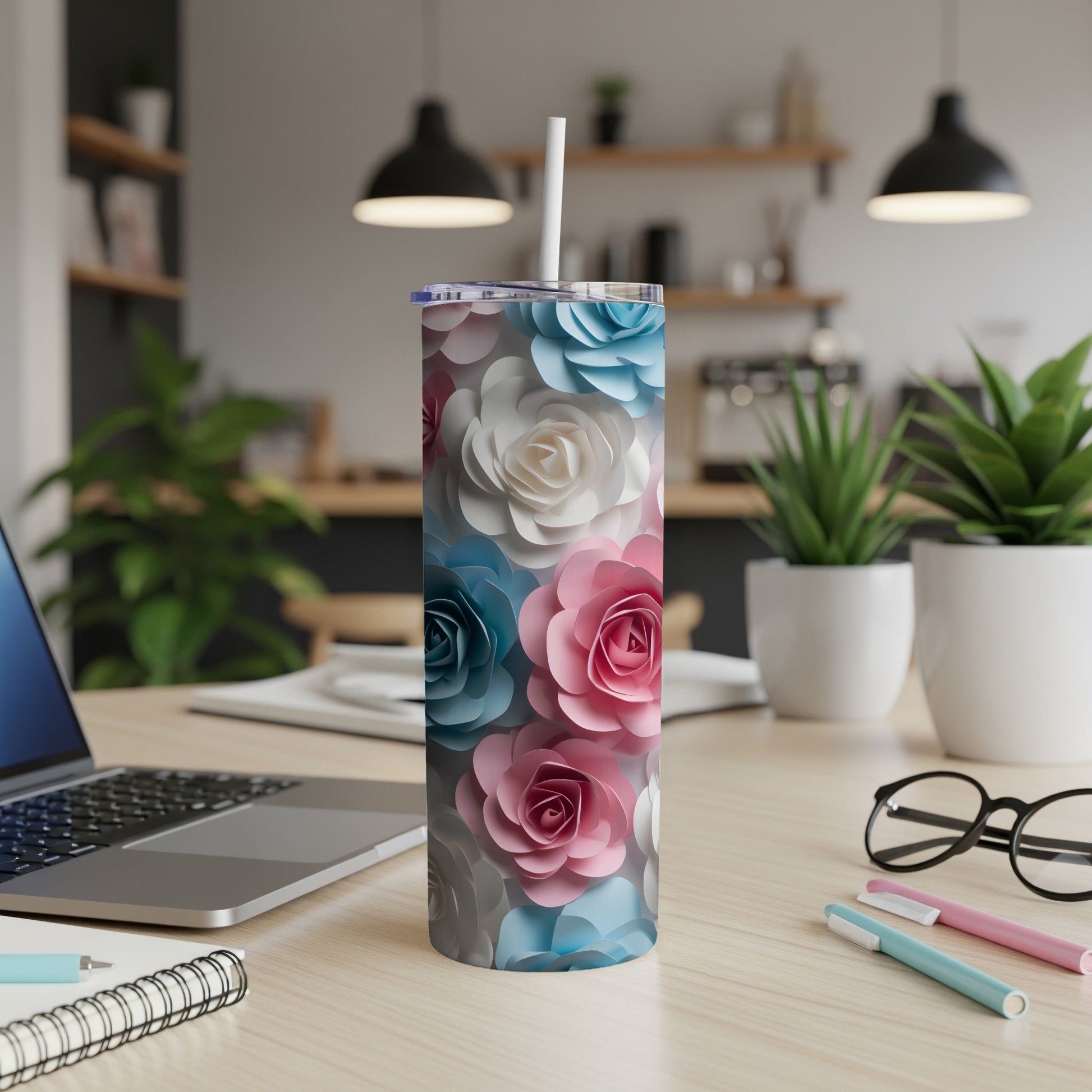 Floral print skinny tumbler with straw on desk with laptop.