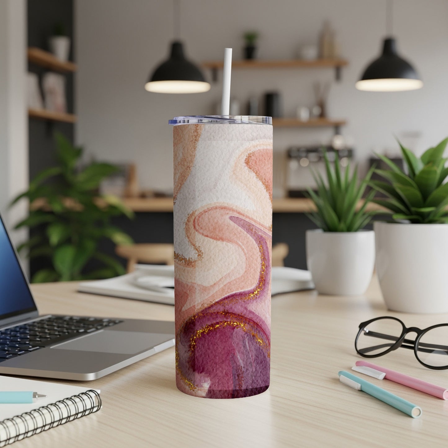 Marble tumbler with straw on a desk with laptop and pens.