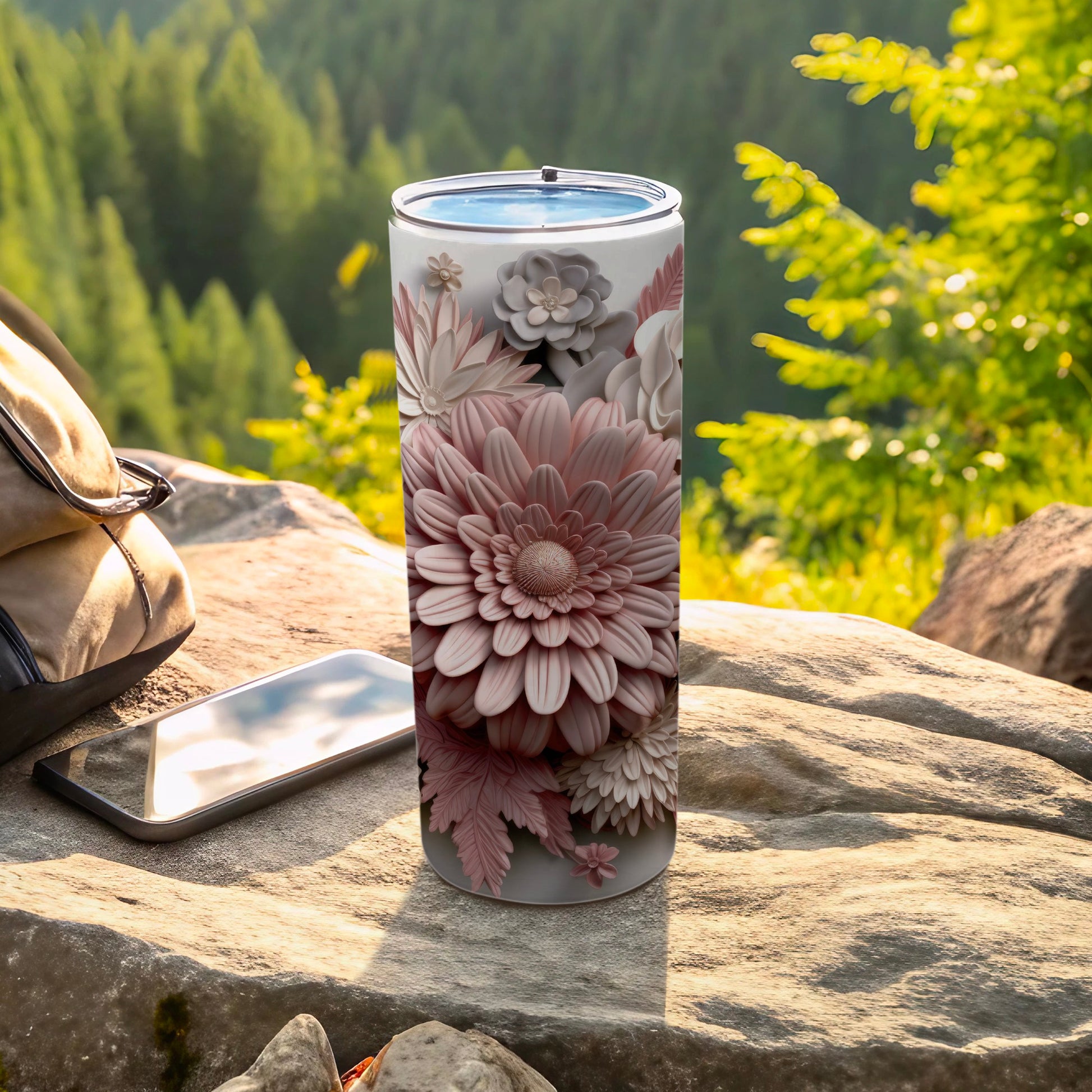 Pink floral tumbler on rock next to phone and backpack in outdoor setting.
