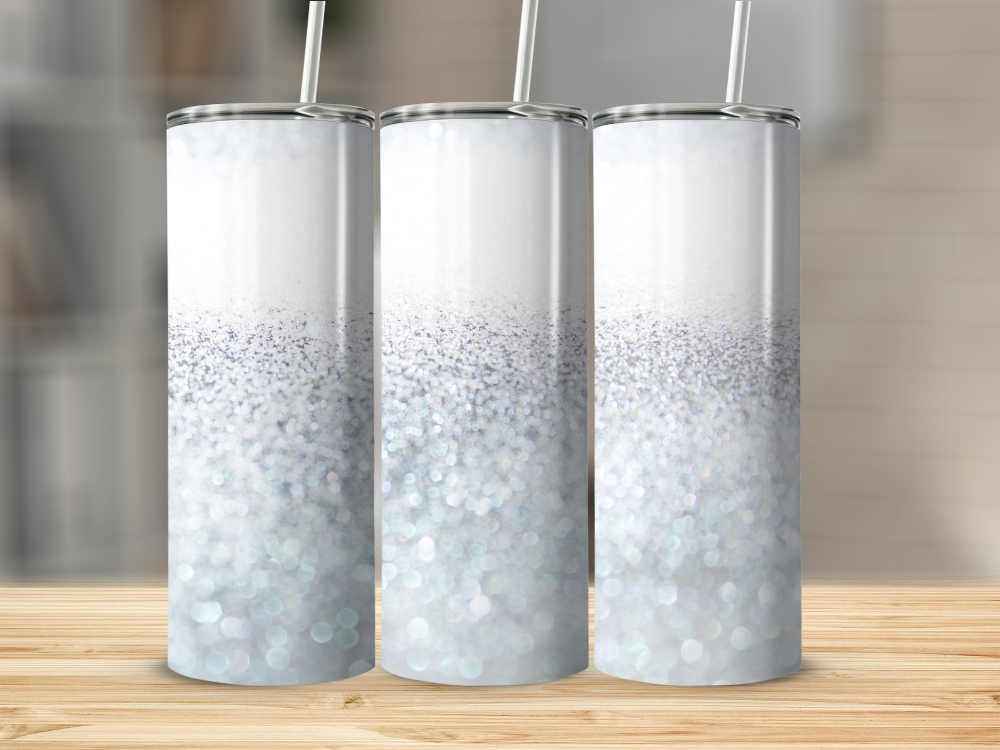 Three glitter-covered tumblers with straws stand on a wooden surface.