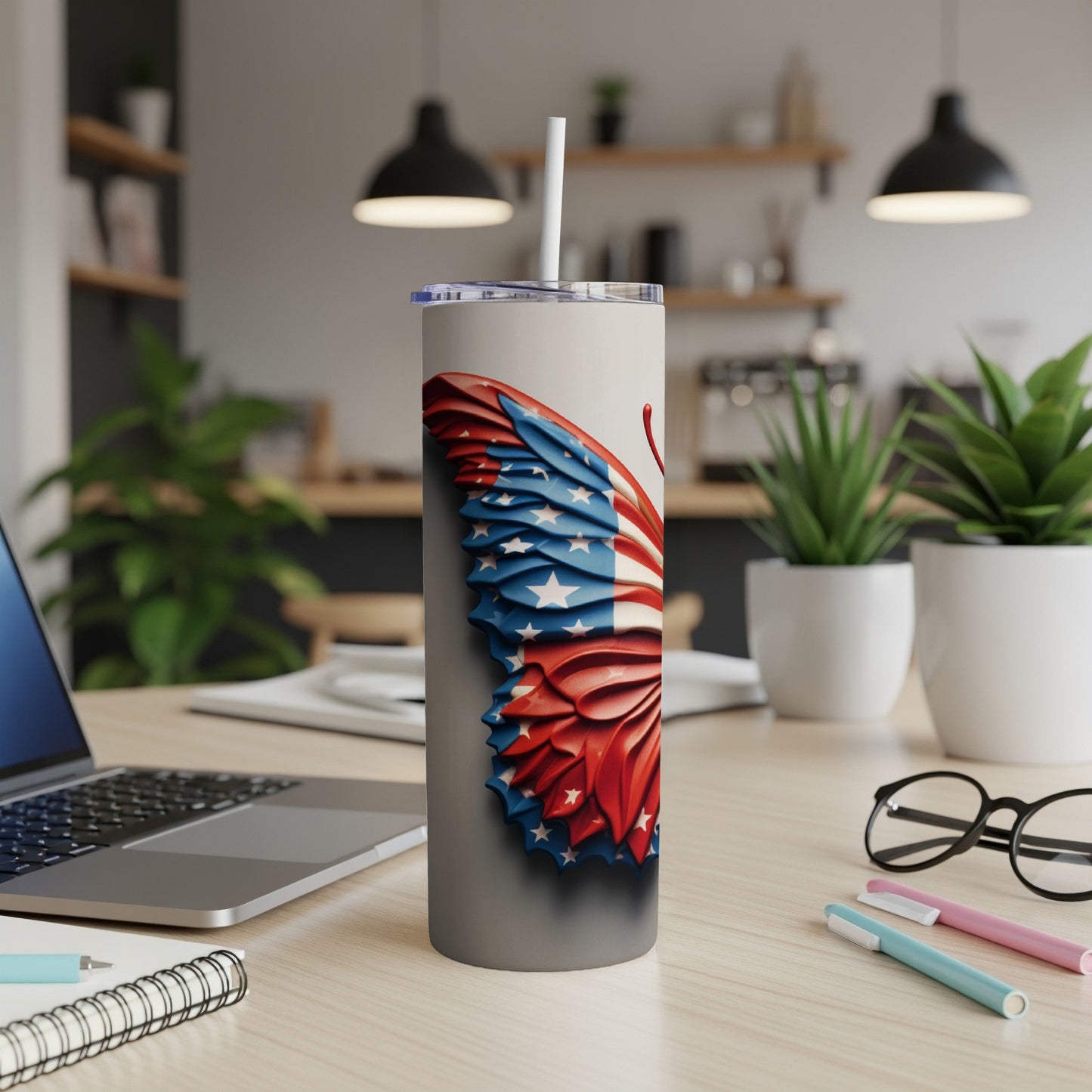 Tumbler with a US flag butterfly design, a straw, and a laptop.