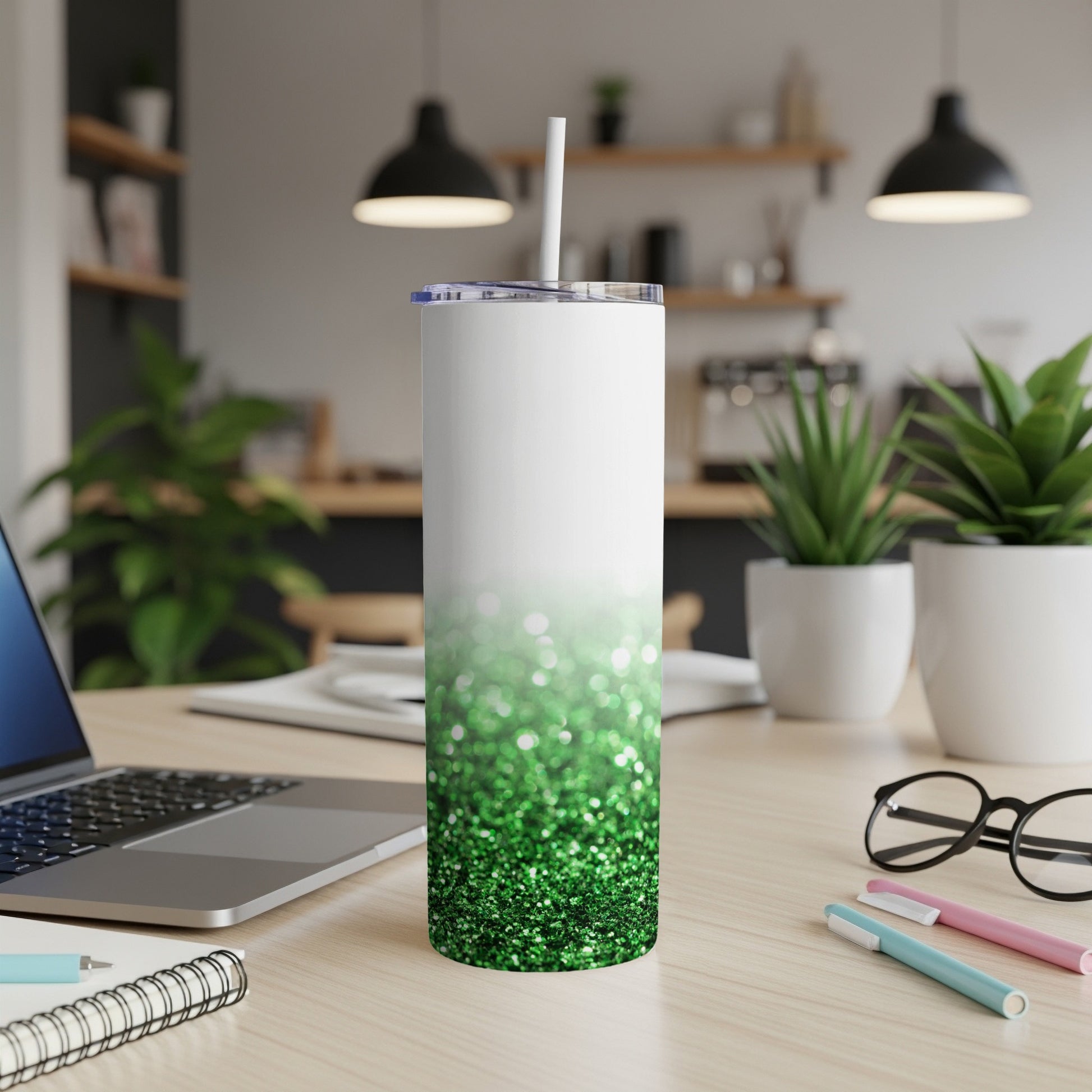White and green glitter tumbler with straw on a desk.