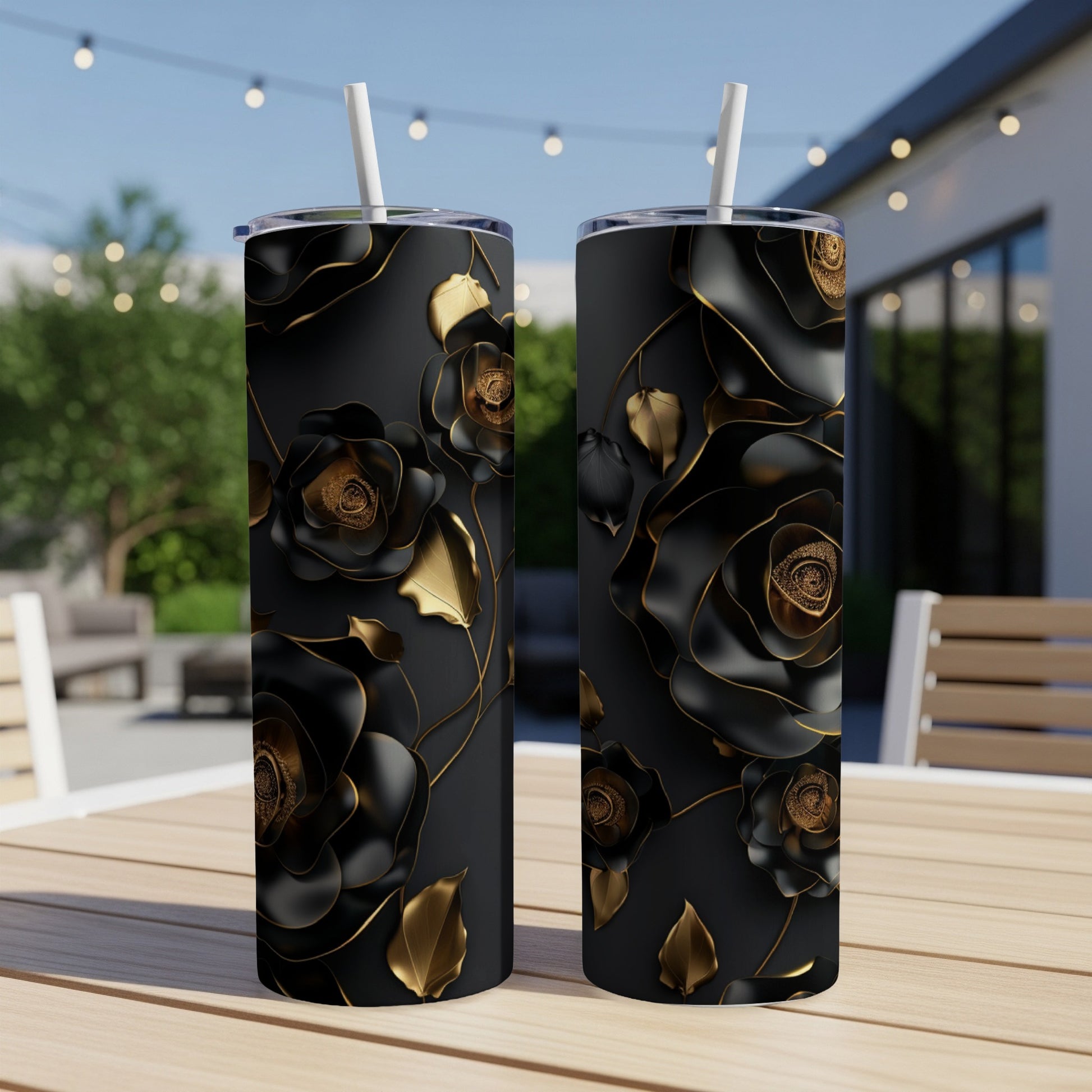 Two black tumblers with gold roses and leaves on a patio table.