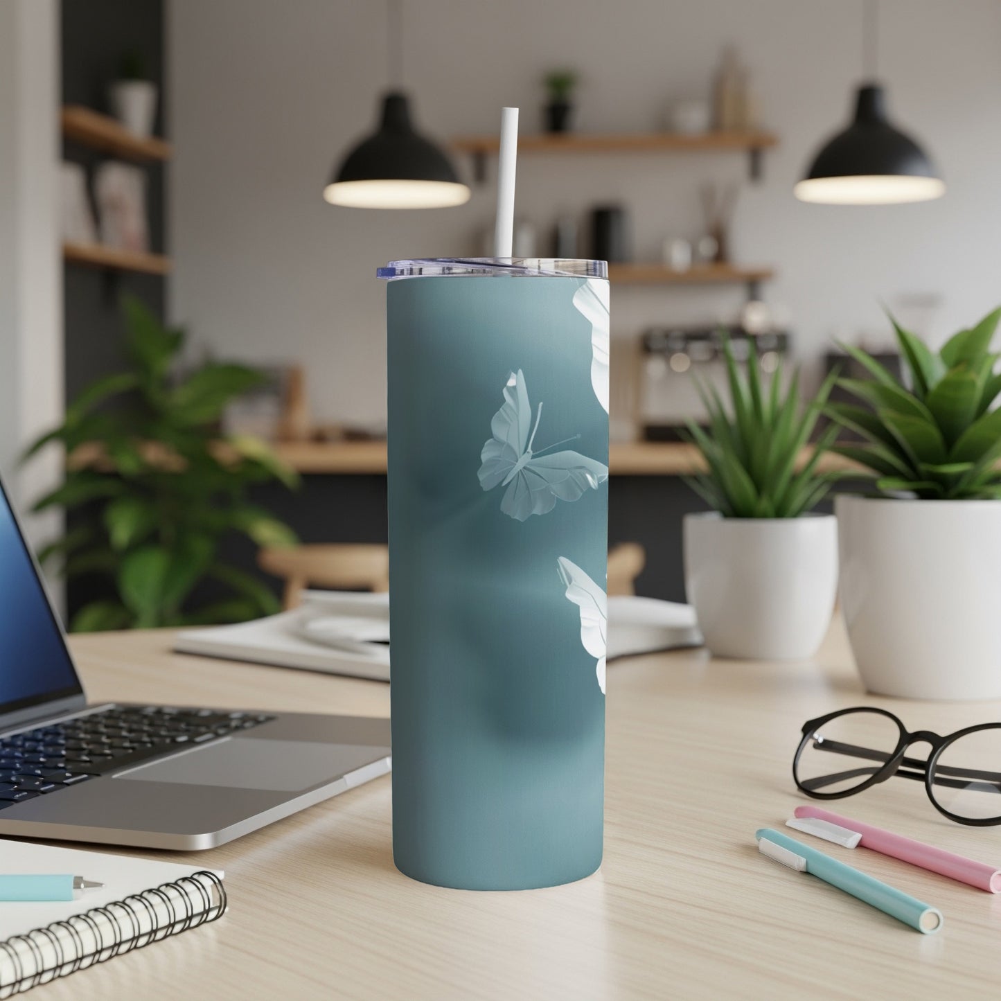Teal tumbler with white butterfly silhouette design, straw, on a desk.