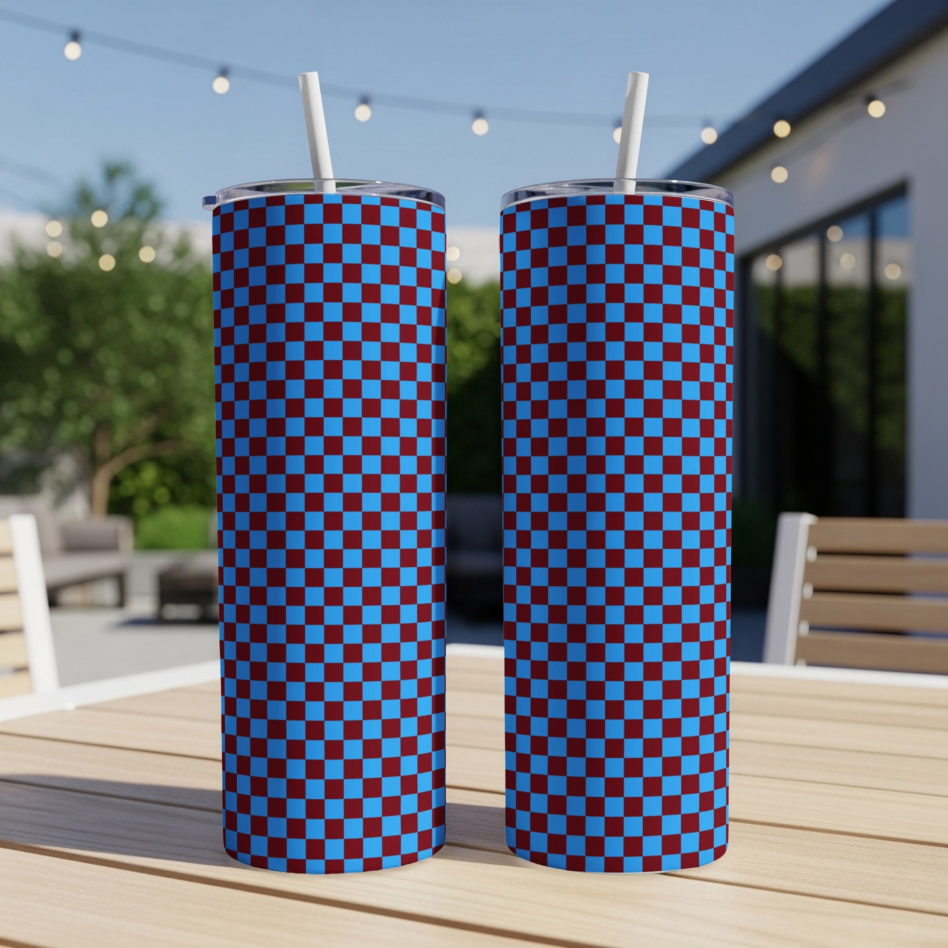 Two blue and maroon checkered tumblers with straws on a wooden table.