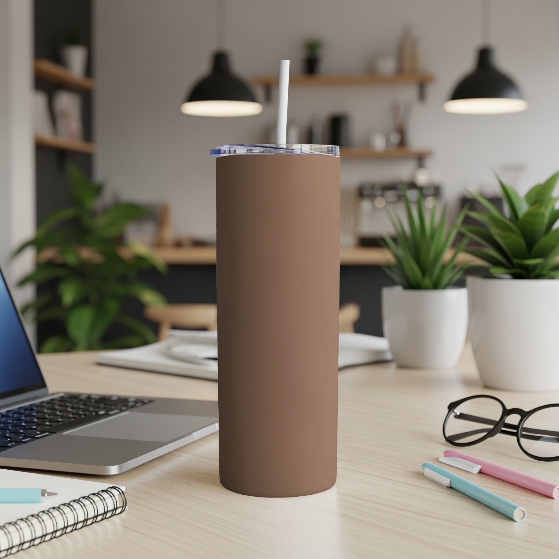 Brown tumbler with straw on desk next to laptop and pens.