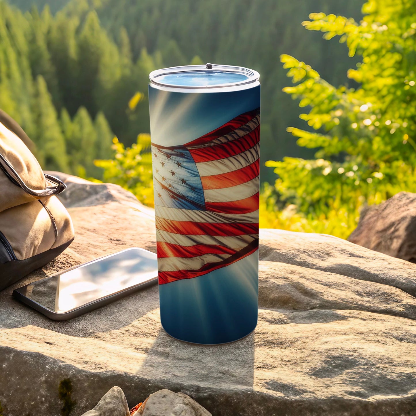 American flag tumbler on rock with backpack and phone.