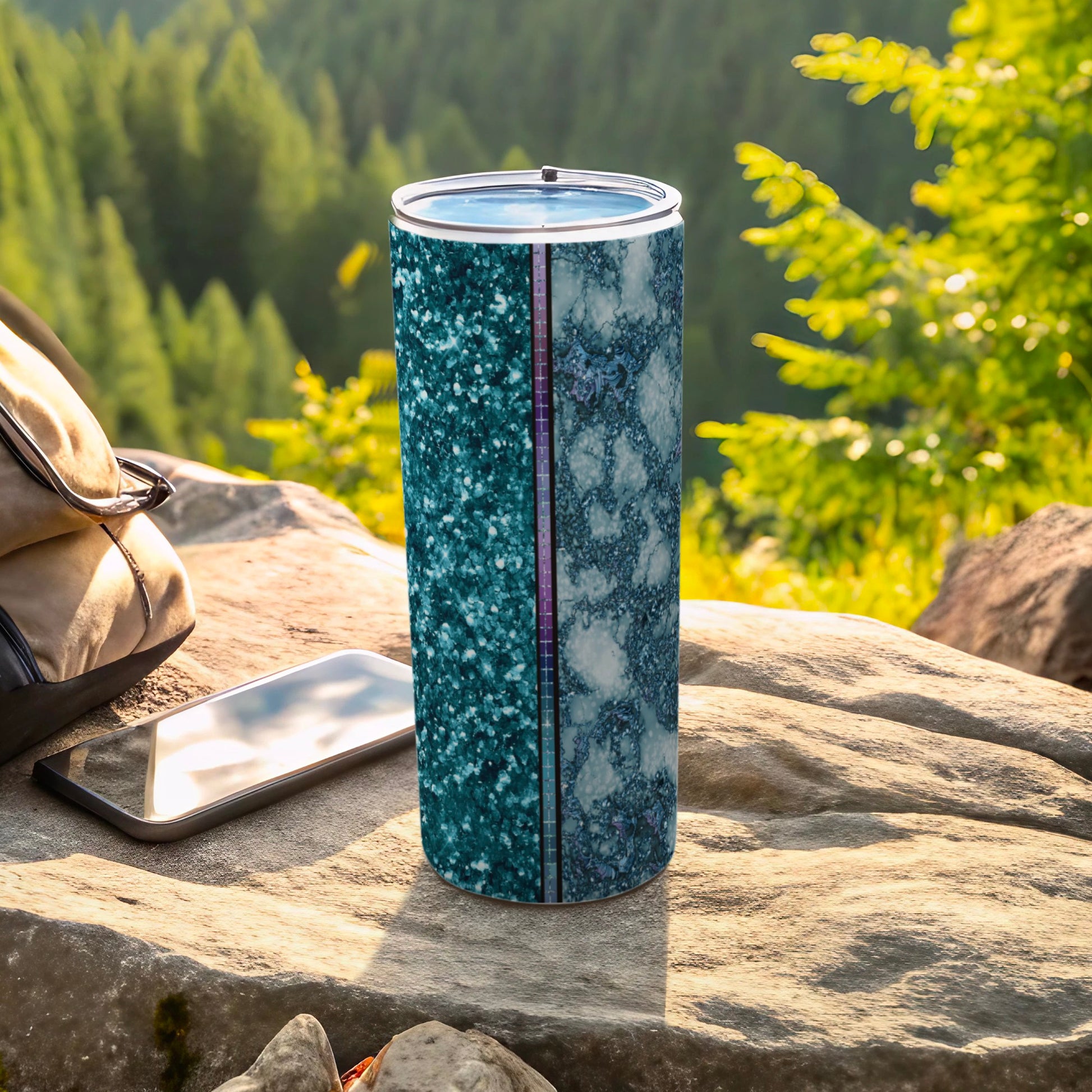 Glittery turquoise and marble pattern tumbler on rock with backpack and phone.