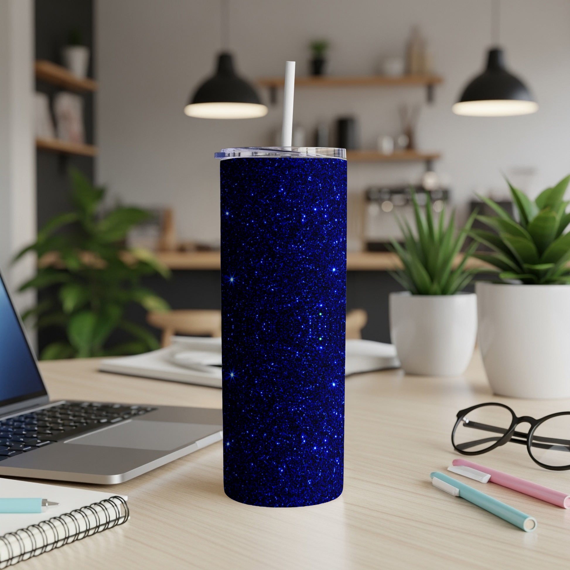 Sparkly blue glitter tumbler with a white straw on a desk.