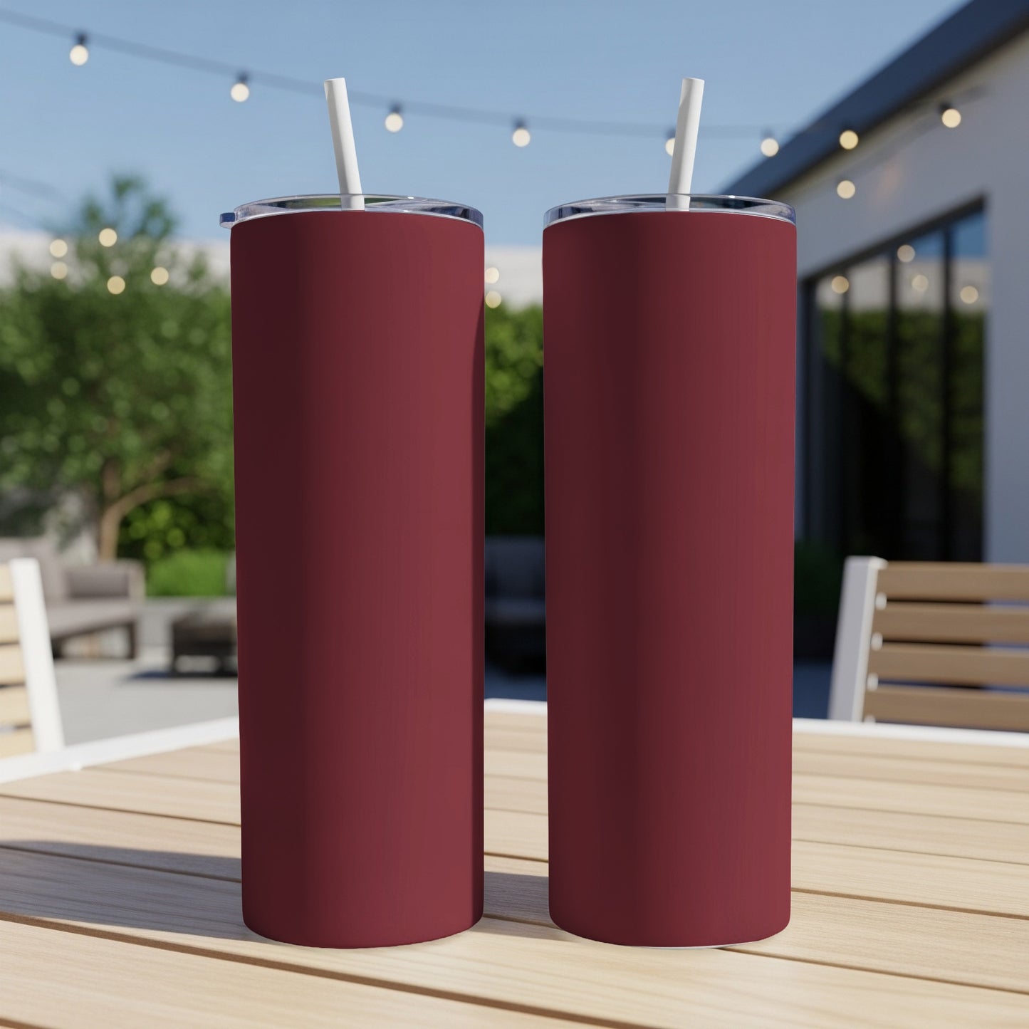 Two maroon tumblers with straws on a wooden table outdoors.
