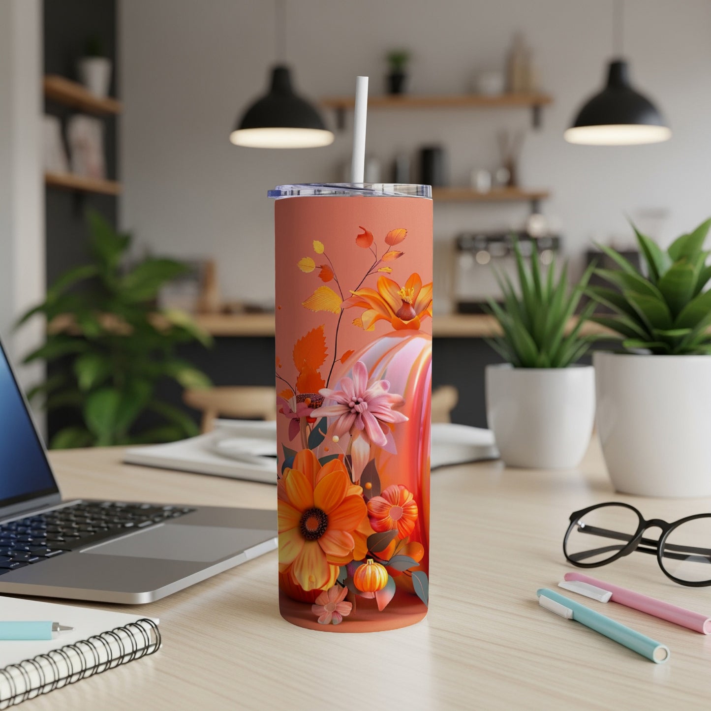 Orange tumbler with a floral pumpkin design and straw, on a desk.