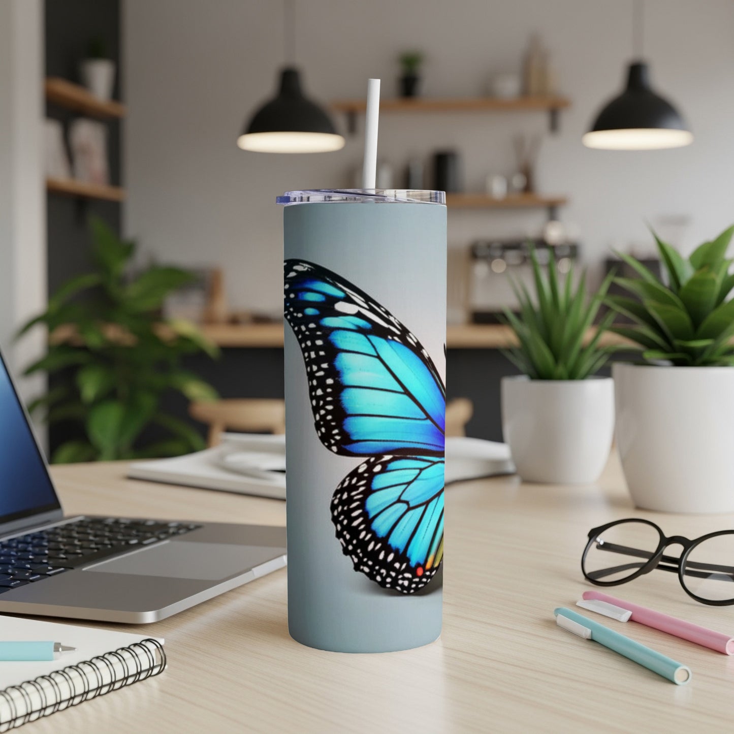 Blue butterfly wing on a silver tumbler with straw on a desk.
