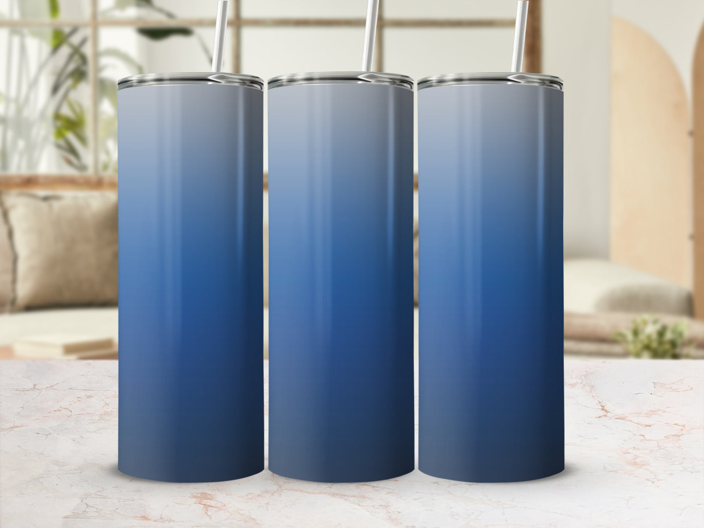 Three gradient blue tumblers with straws on a marble surface.
