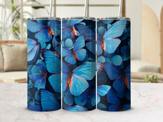 Three blue butterfly print tumblers with straws on a marble surface.