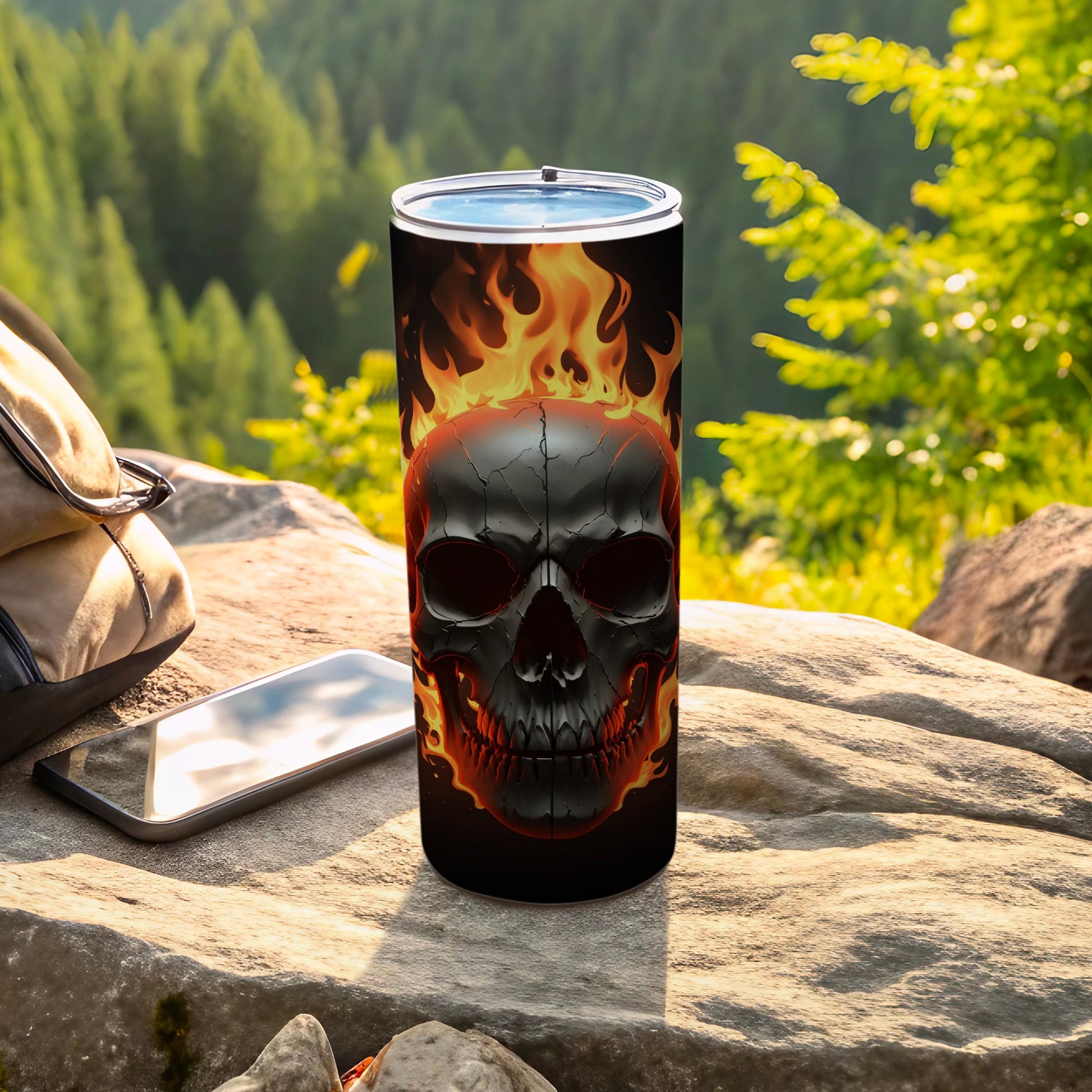 Black tumbler with fiery skull design, on rocks outdoors.