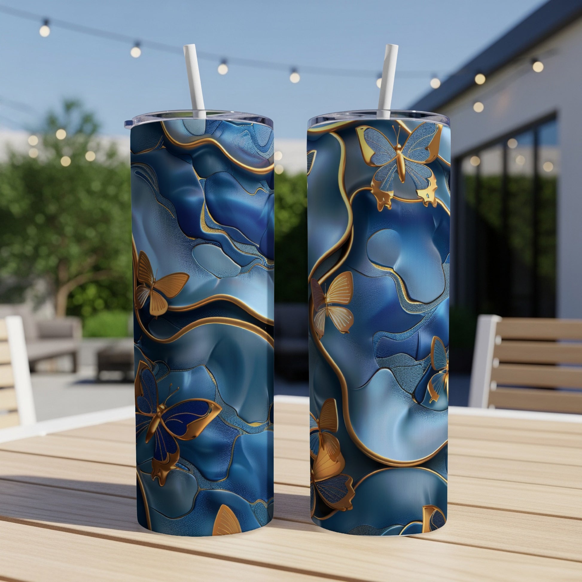 Two blue tumblers with gold butterfly and swirling patterns on an outdoor table.