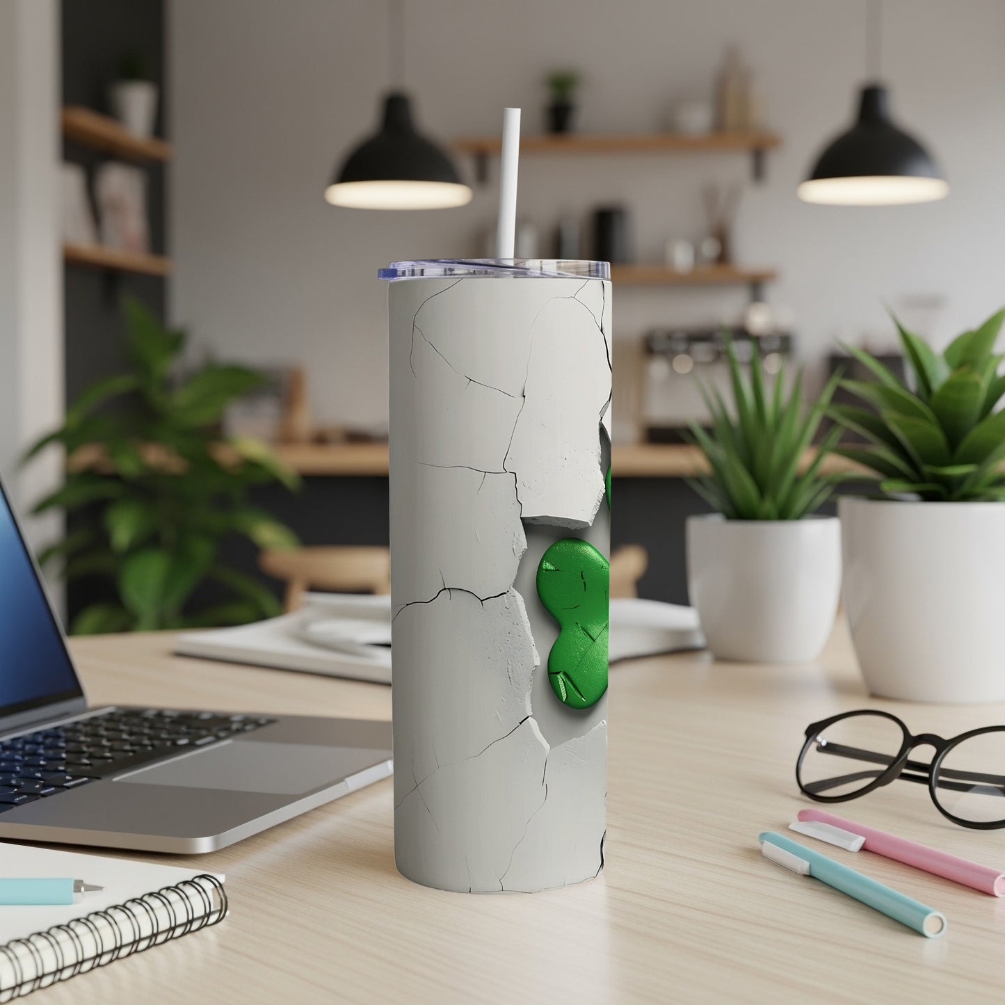 White cracked tumbler with green alien graphic and straw on desk.