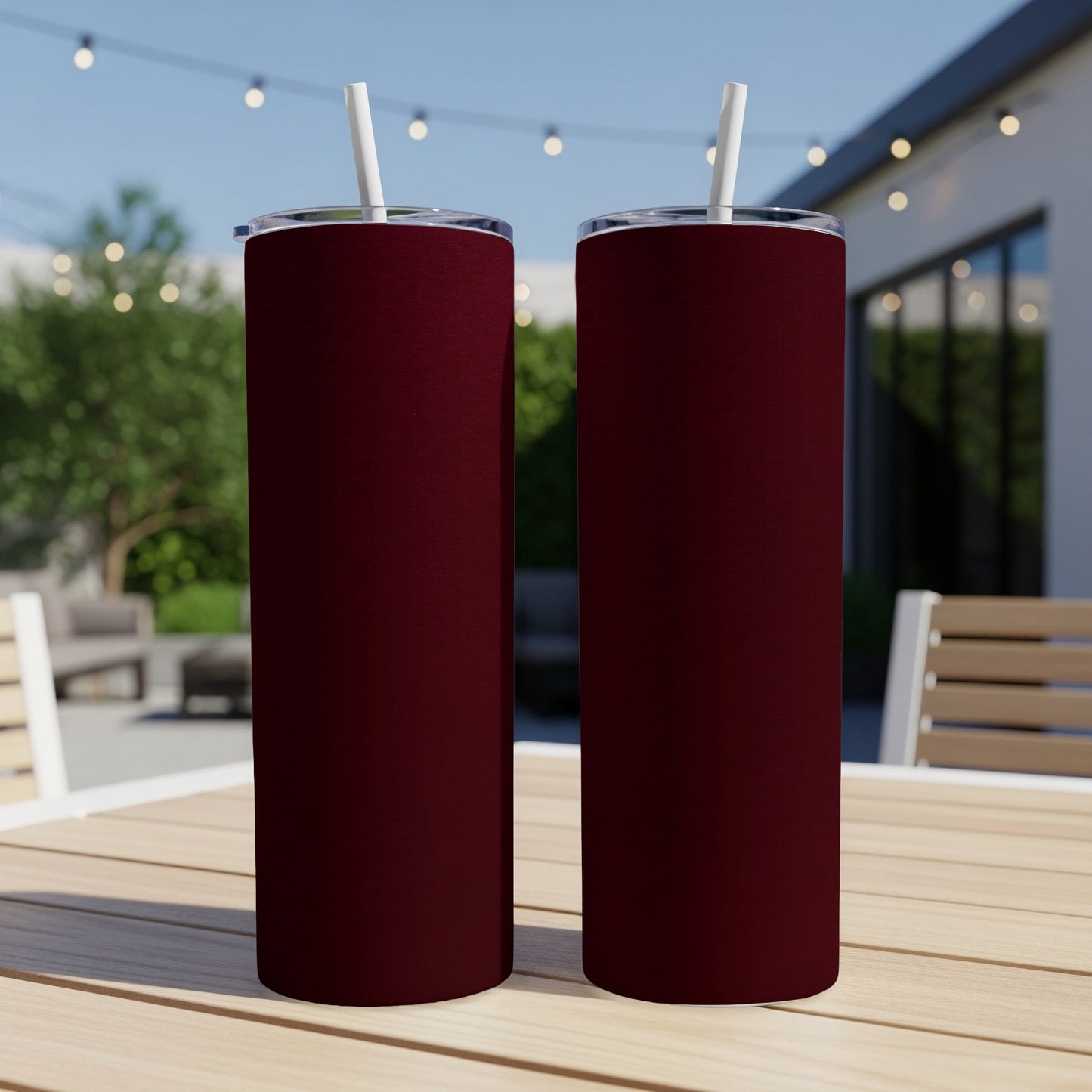 Two maroon tumblers with white straws on a wooden table outdoors.