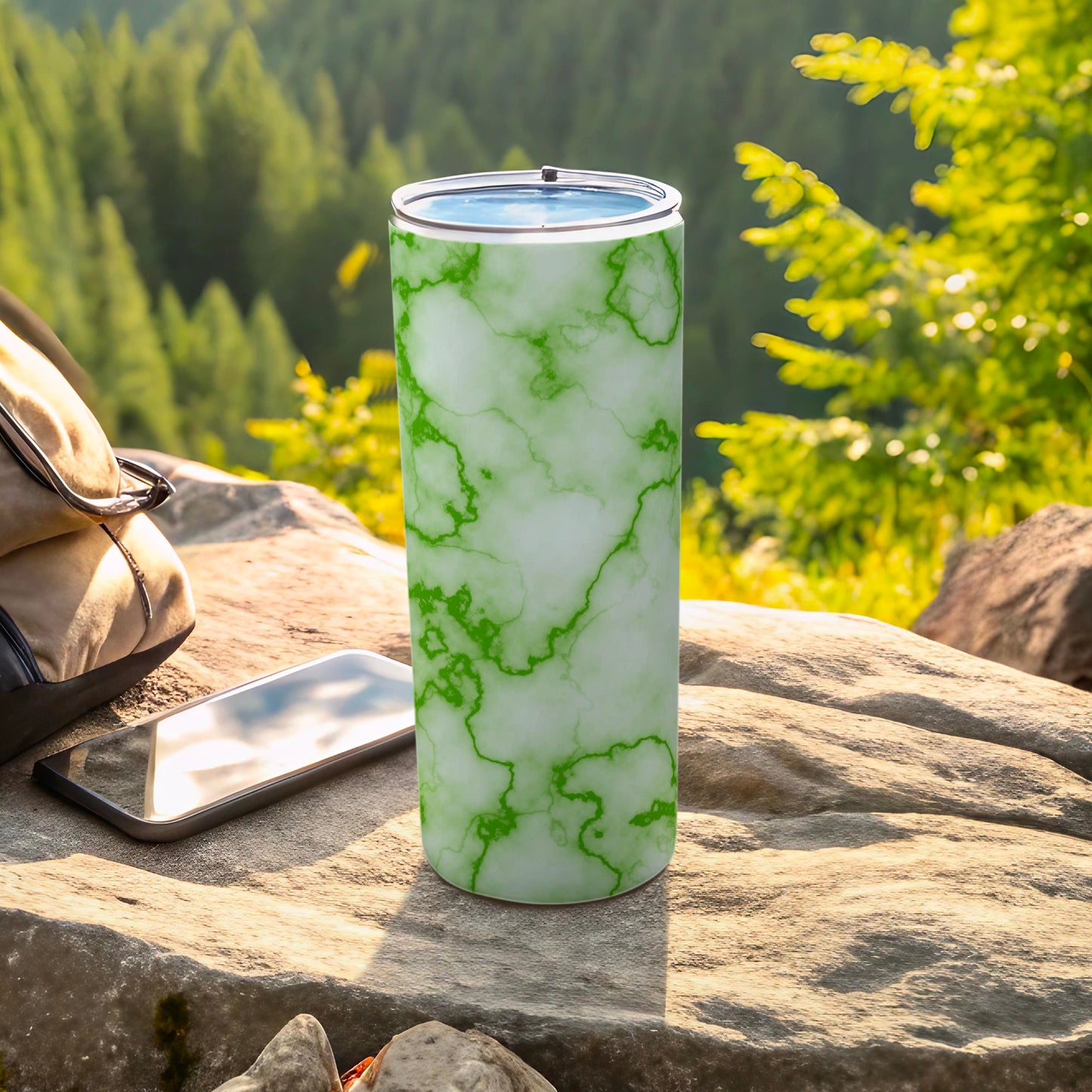 Green marble patterned tumbler on rocky surface with phone and backpack.